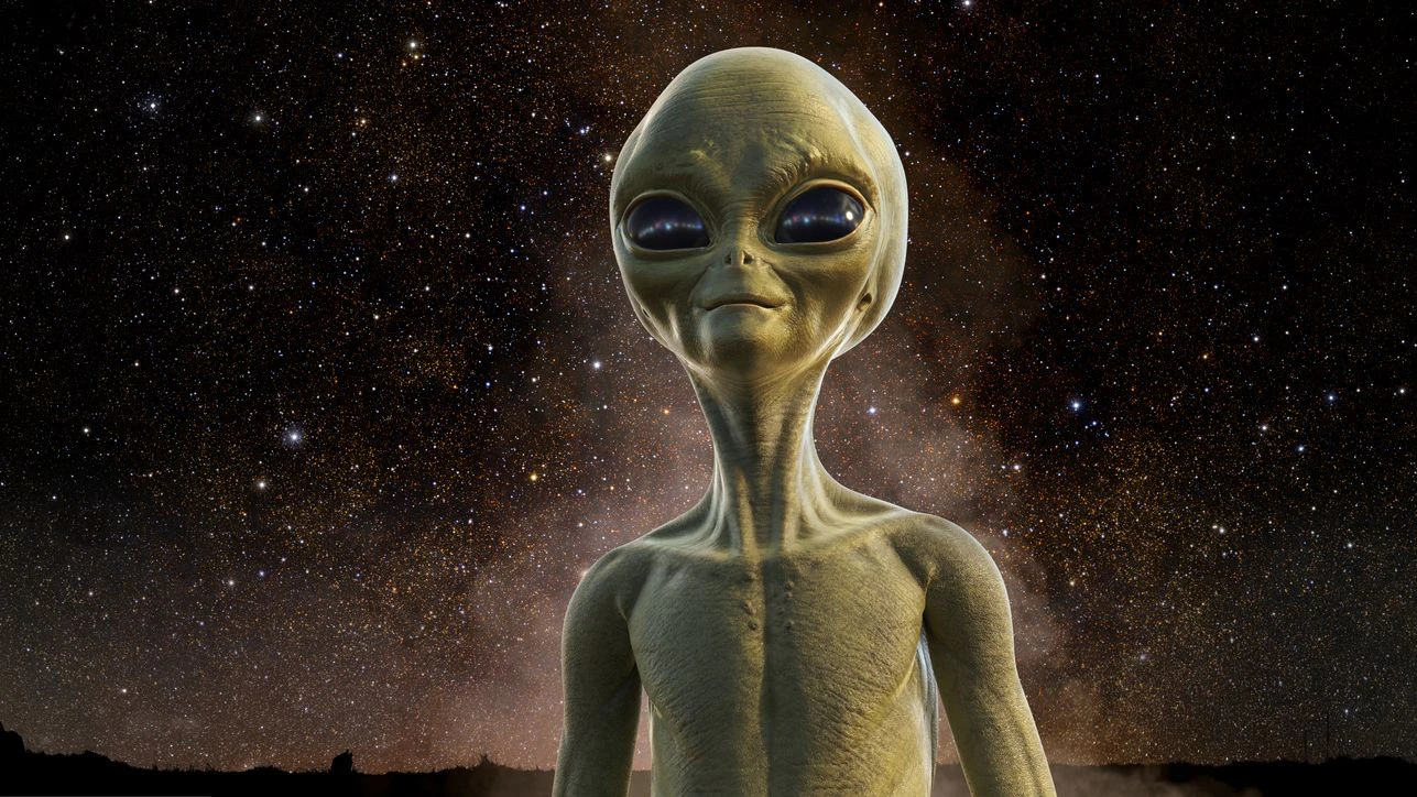 A portrait of the head and upper torso of a yellow-green extra terrestrial being standing under a clear starry sky with some background haze.  With copy space.