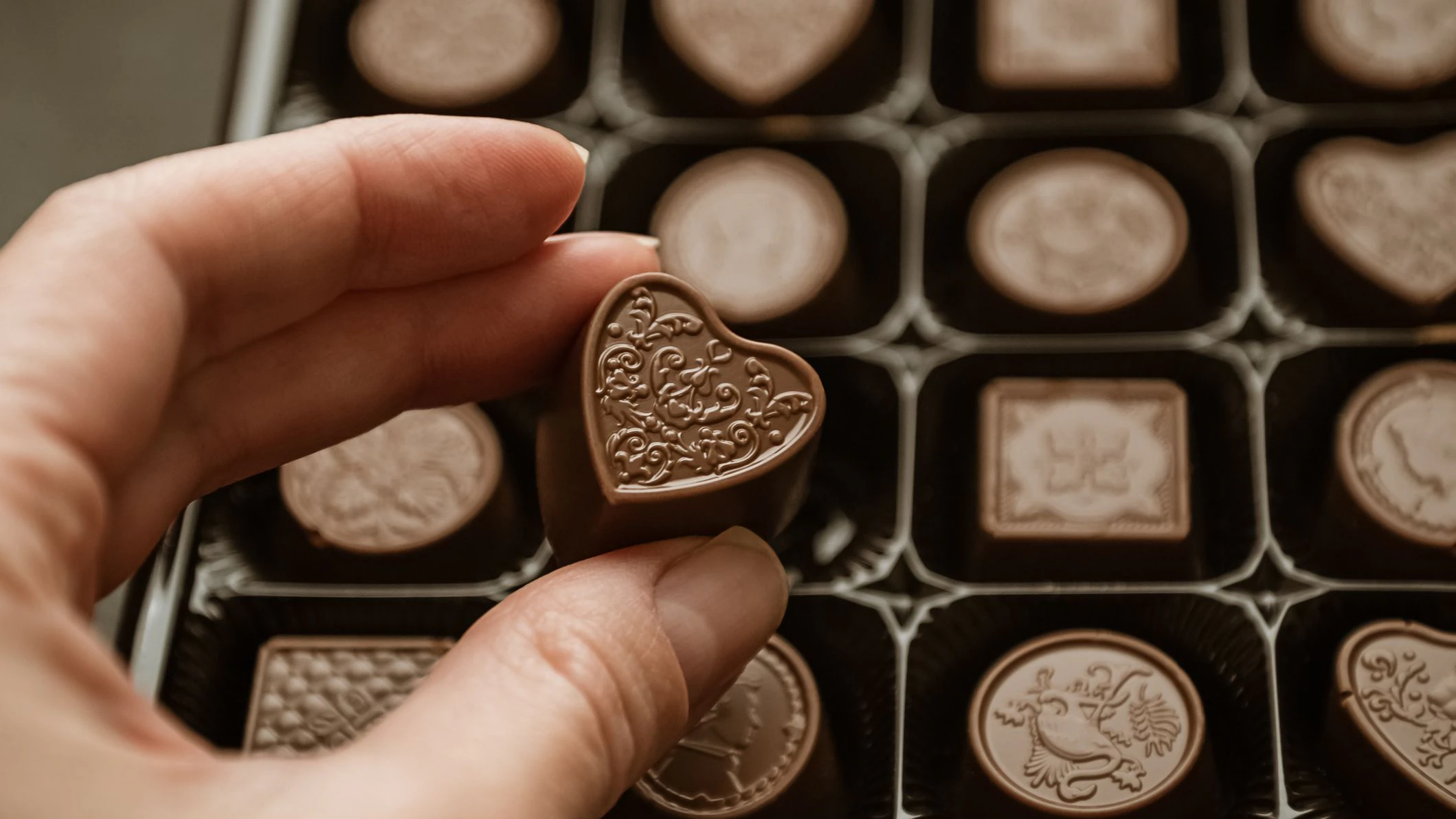 Person taking heart-shaped chocolate sweet from candy box