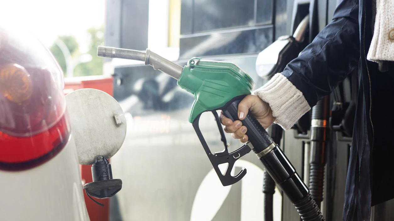 Close-up of a female hand holding a green fuel pump nozzle, refueling a car at a gas station.