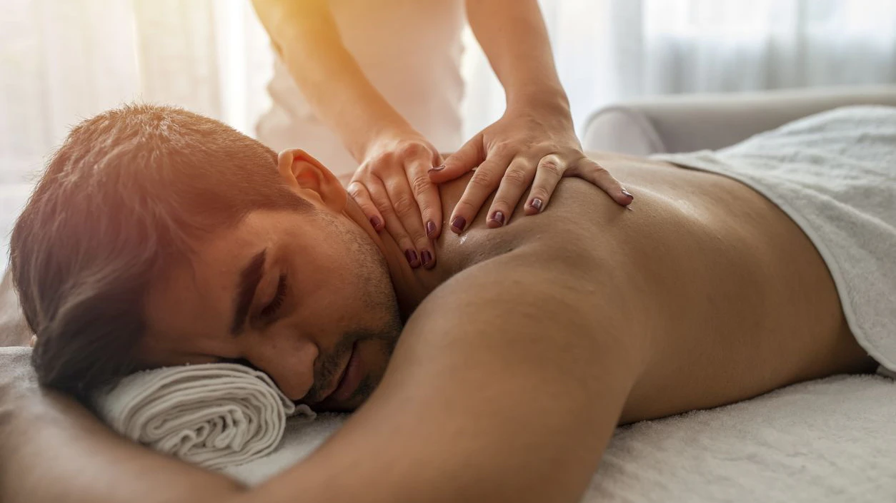 Young man is enjoying massage on spa treatment. Man relaxing in a wellness center. Young man receiving massage at spa salon. Hands of a masseuse working. Handsome man at the spa