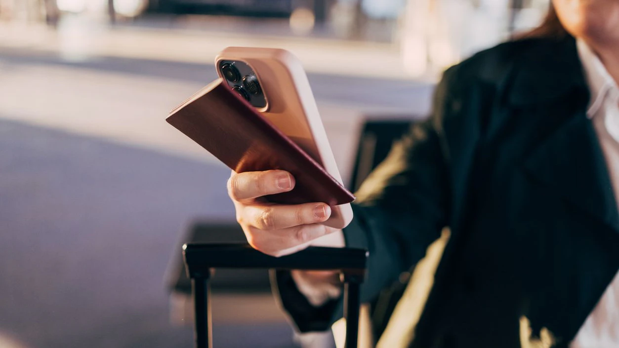 Close-up of a woman holding a passport and smartphone while sitting in an airport terminal. The scene suggests travel and modern connectivity, capturing a moment of anticipation before a journey.