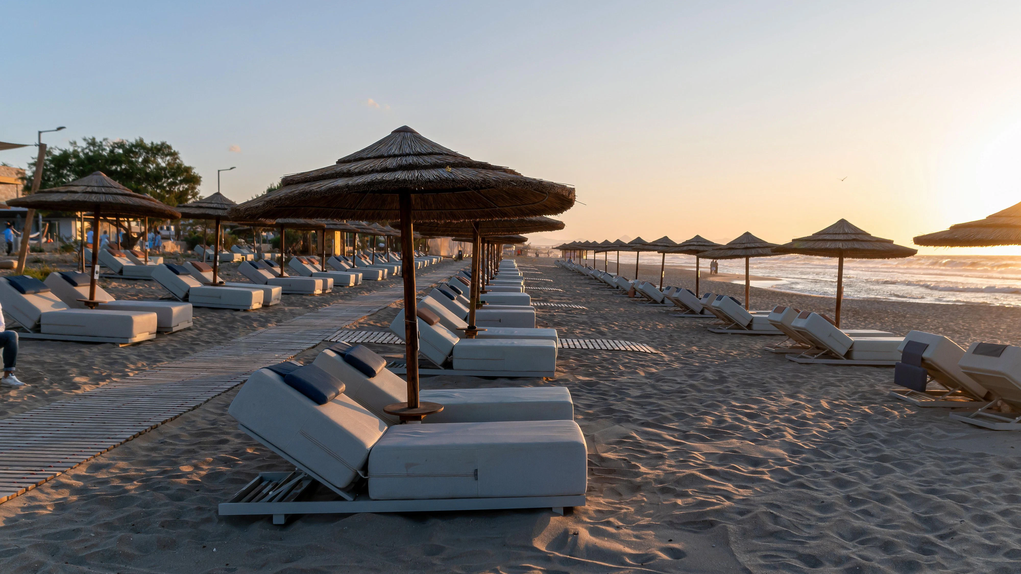Lounge chairs and thatched umbrellas create a tranquil setting on Crete's beach at sunset.