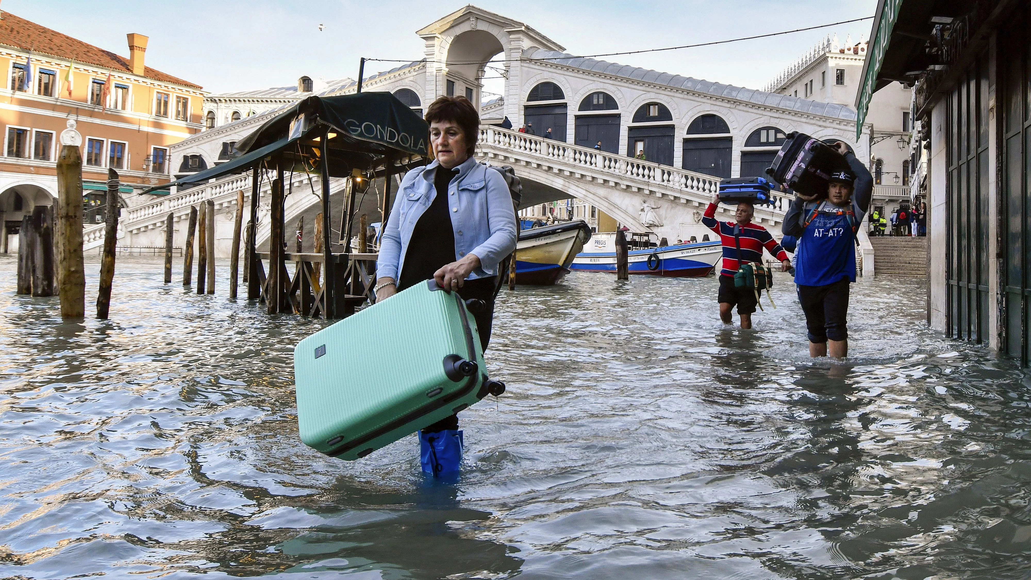 People carry their luggage as they wade through water during a high tide of 1.44 meters (4.72 feet), near the Rialto Bridge, in Venice, Italy, Monday, Dec. 23, 2019. Venice is facing more intense floods on Monday, while it battles to recover from the exceptional high tide that hit it in November, causing massive damages. (AP Photo/Luigi Costantini)
