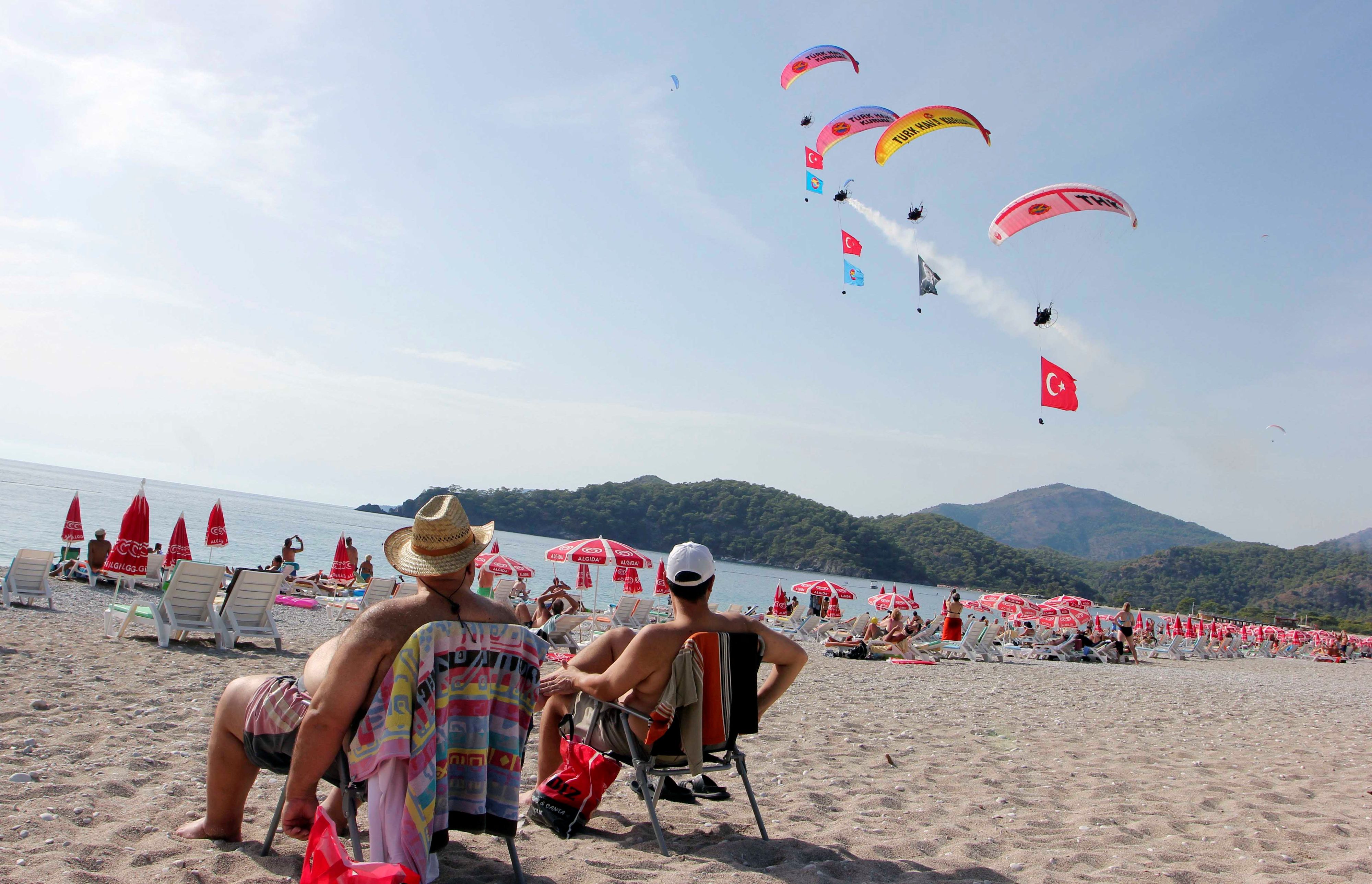 Touristen verfolgen die Internationalen Oludeniz Air Games und genießen das sonnige Wetter an einem Strand in Fethiye in der Provinz Mugla, Türkei.