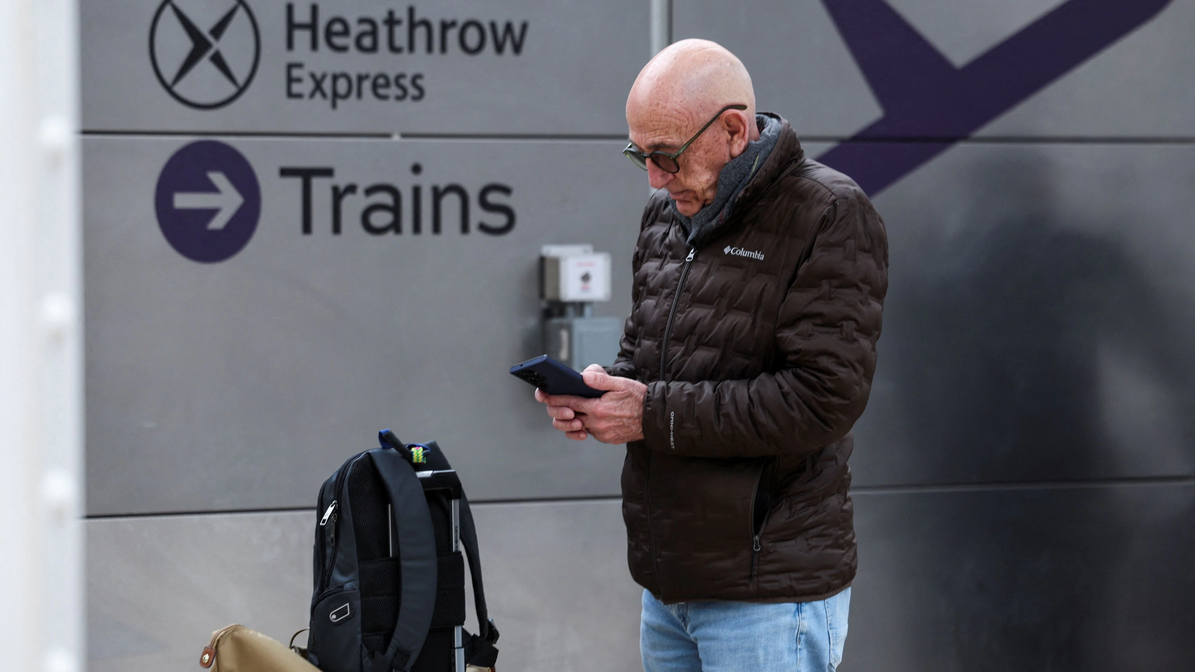 A man looks at his smartphone near the Heathrow Express platform at the Paddington railway station, after a fire at a electrical substation wiped out power at the Heathrow International Airport, in London, Britain, March 21, 2025. REUTERS/Isabel Infantes