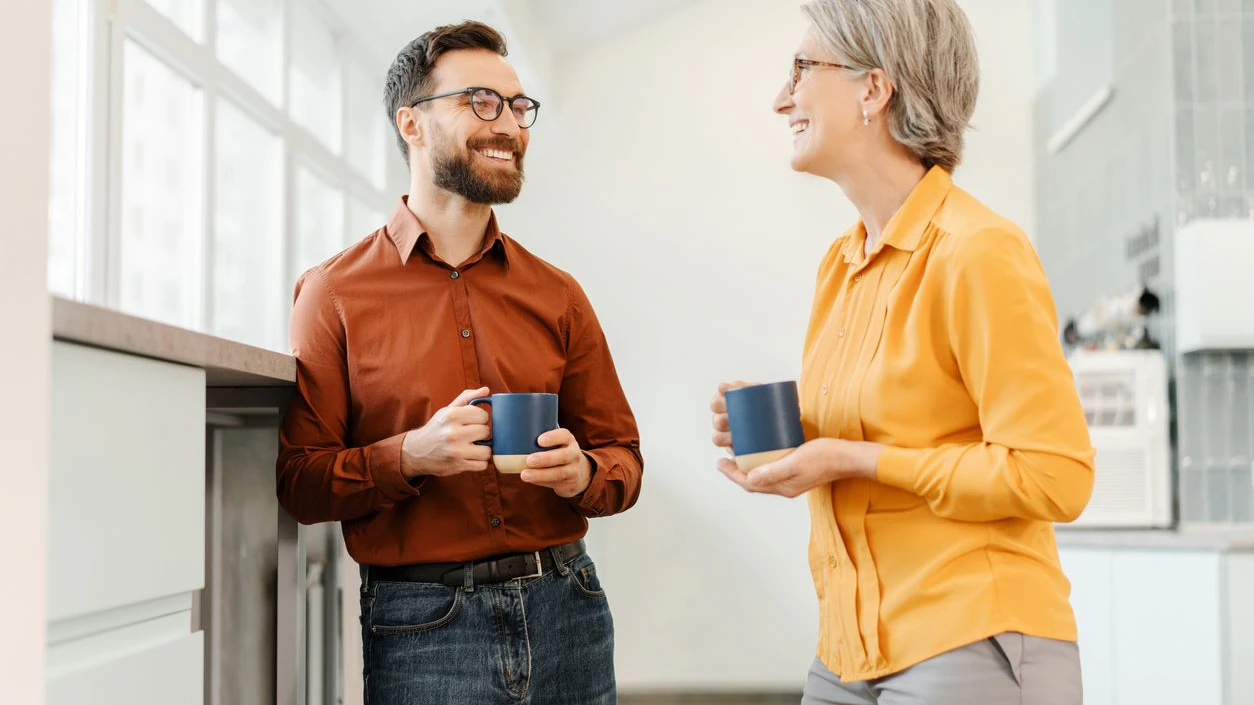 Overjoyed business colleagues drinking coffee together in modern office. Happy senior woman and bearded man having break. Business concept