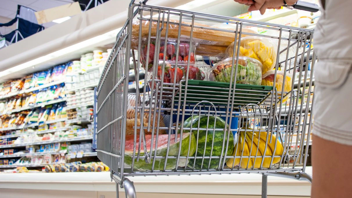 Caucasian woman pushing a shopping cart full of fruits and vegetables inside a supermarket