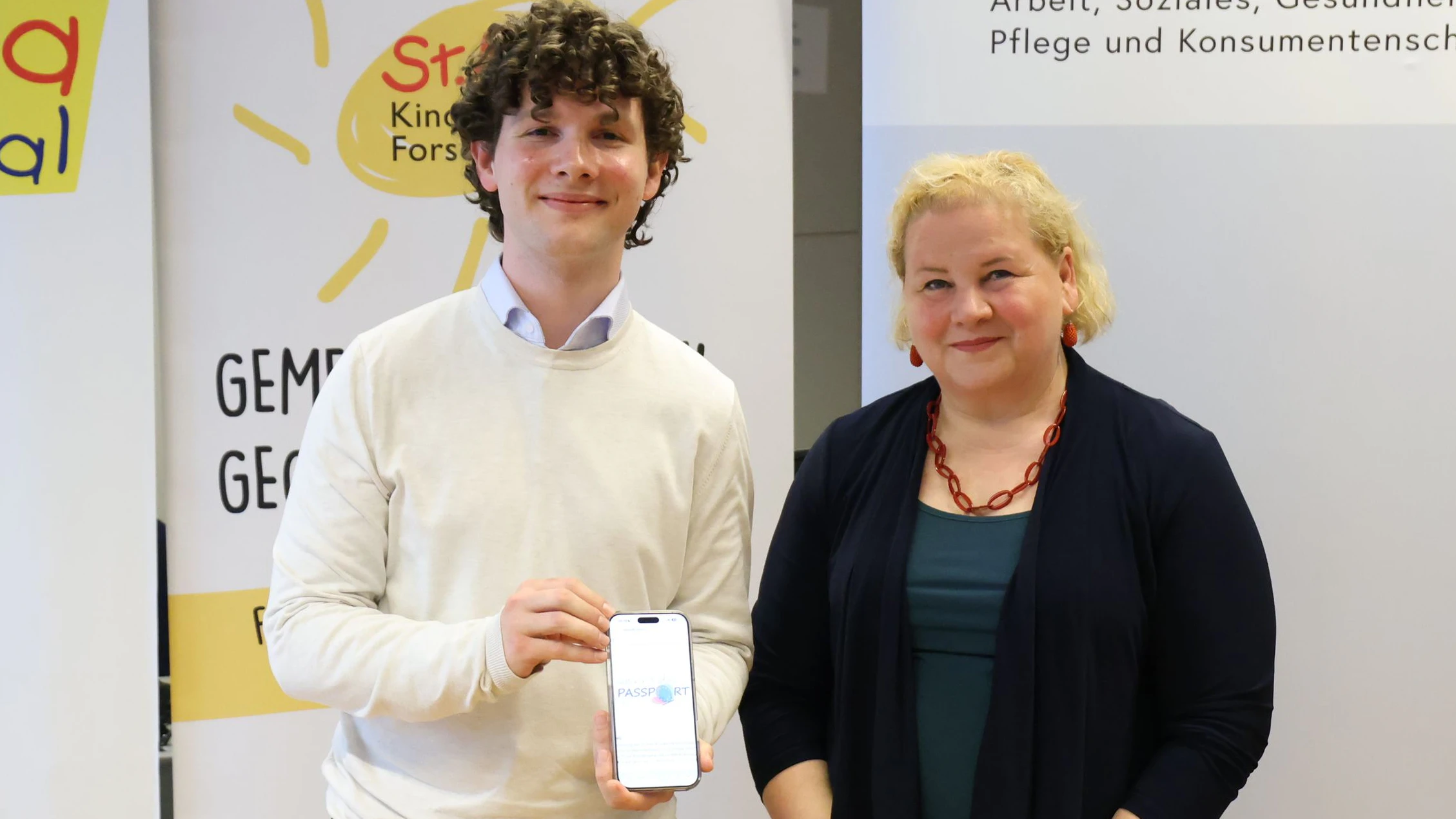 Julian zeigt Gesundheitsministerin Schumann den "Survivorship Passport" am Handy.