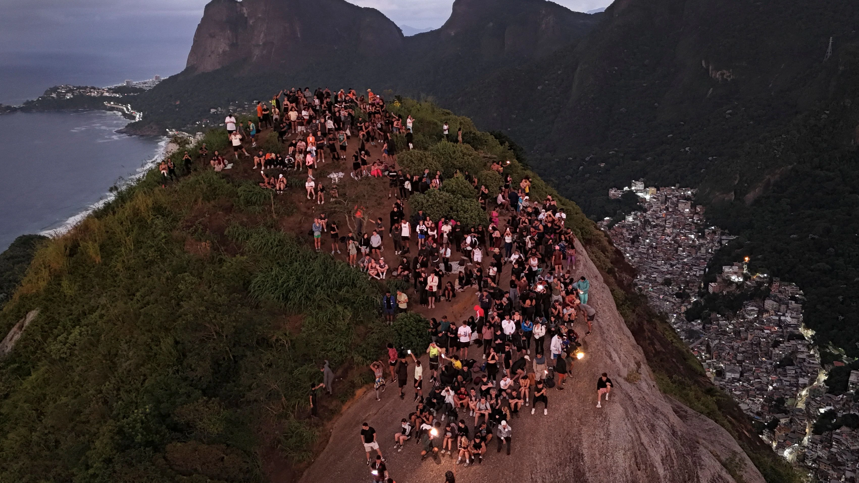 Tourists watch the sunrise from Morro Dois Irmaos above the Vidigal favela, a day after a police operation in Rio de Janeiro, Brazil, on April 21, 2026. A police operation against drug trafficking took place in the Vidigal favela early morning on April 20, in the touristy south zone of Rio de Janeiro, during which around 200 tourists were temporarily stranded on Morro Dois Irmaos, from where they were later evacuated unharmed by local tour guides. (Photo by Pablo PORCIUNCULA / AFP)