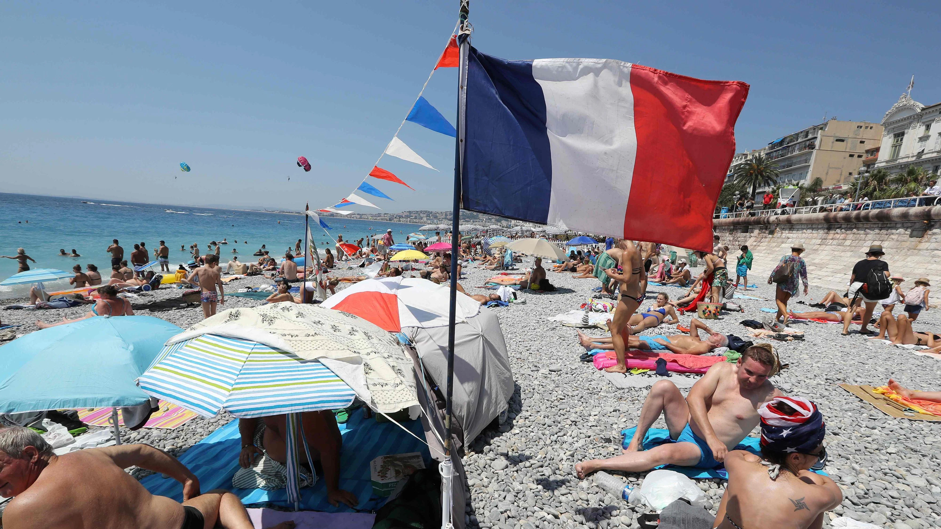 People lay on the beach where supporters of France's national football team planted French flag in Nice, a few hours prior to the Russia 2018 World Cup final football match against Croatia, on July 15, 2018. / AFP PHOTO / Valery HACHE