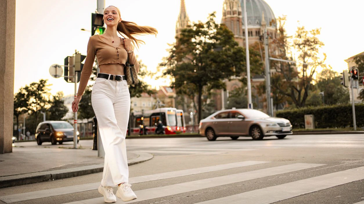 Young woman happily walking across a city street with architecture in the background at sunset