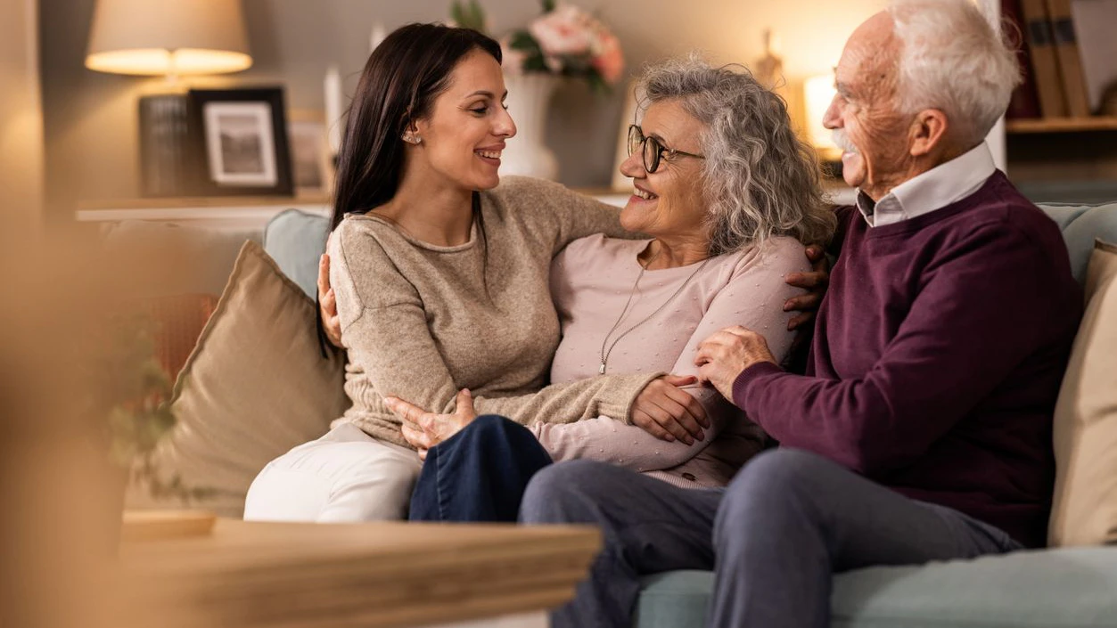 Daughter visiting her mother and father while they sitting on ouch at home in living room