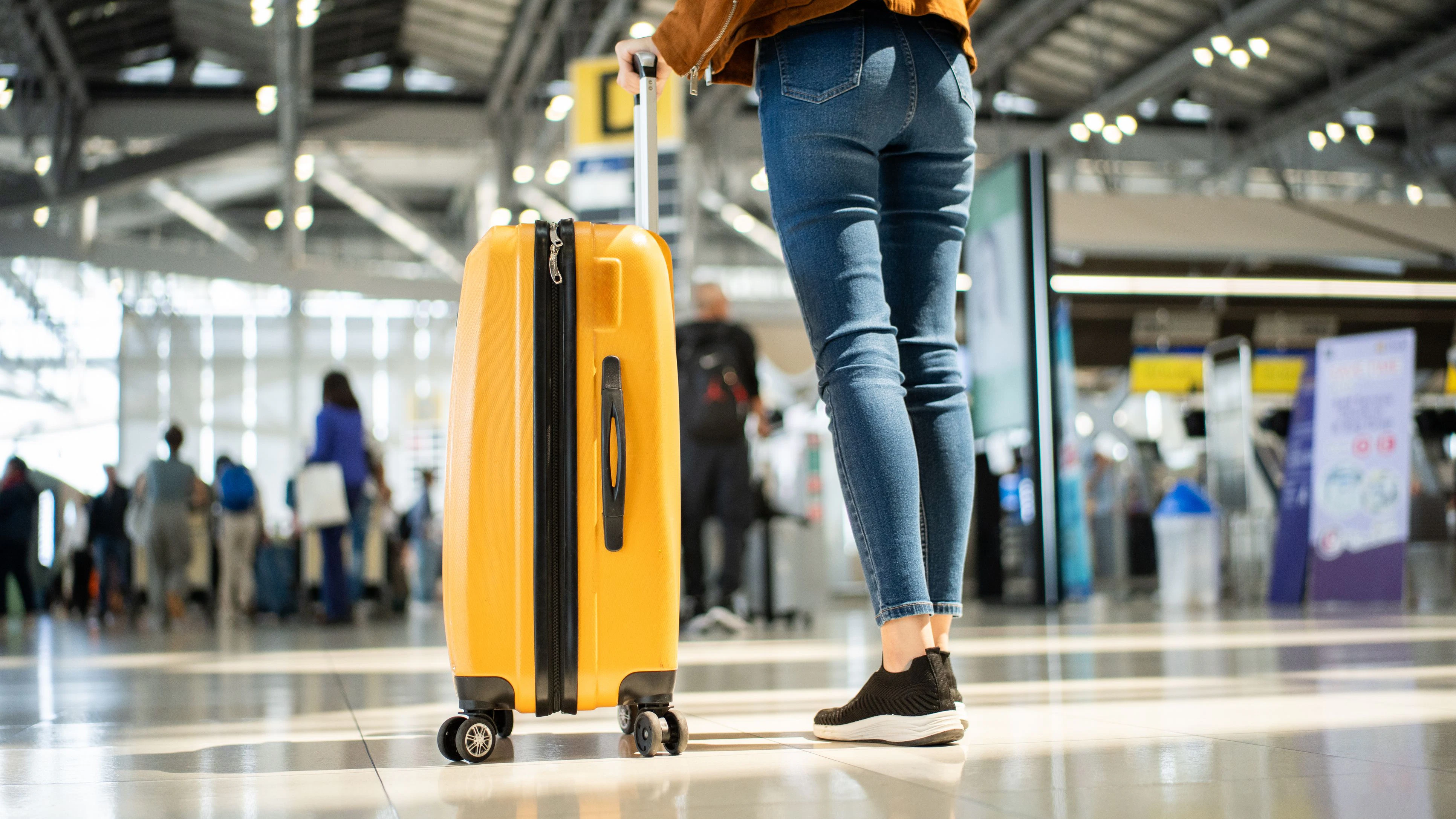 Close up of unrecognized woman tourist walking with her luggage through international airport terminal during holiday trip, female tourist rolling suitcase alone.
