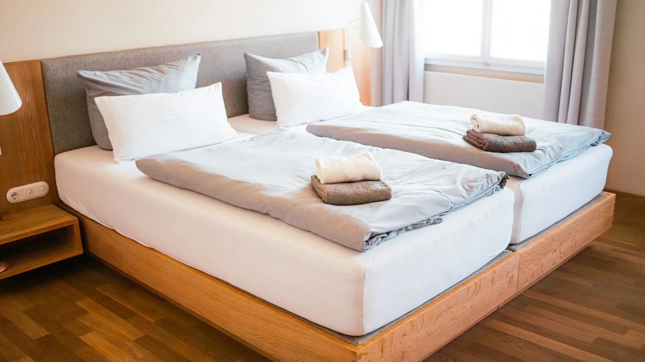 Spacious hotel room showcasing a neatly made double bed. Soft linens and fresh towels create an inviting atmosphere, perfect for relaxation. The minimalist design exudes comfort and modernity.