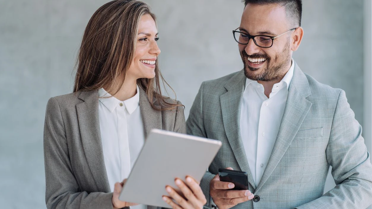 Shot of a two confident business persons talking in the work place. Two colleagues using a digital tablet while walking in a modern office. Businessman and businesswoman in meeting discussing business strategy. Business coworkers working together in the office.