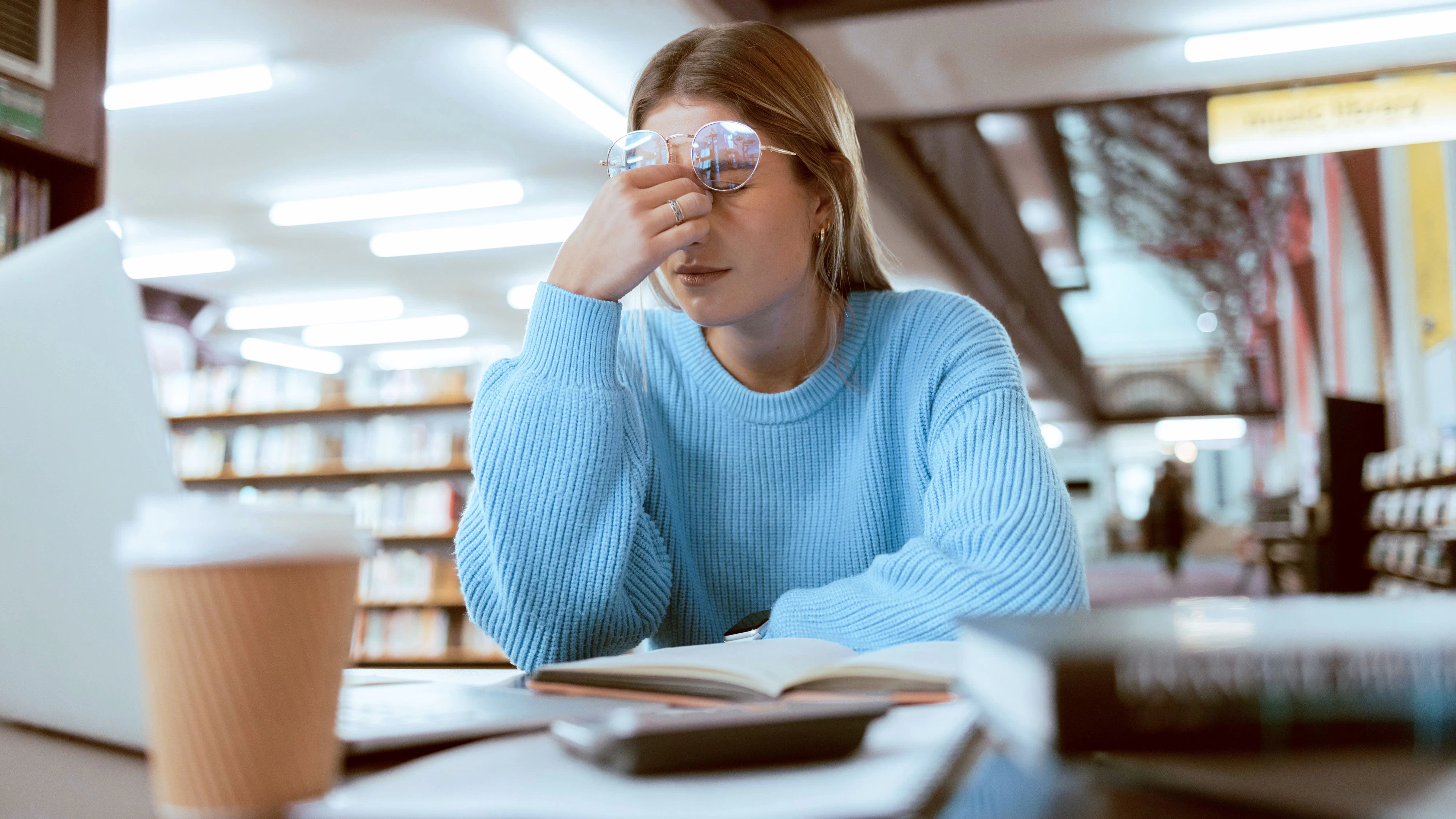 Woman student, fatigue with headache and university burnout, stress for paper deadline or study for exam in library. Campus, college and tired studying with scholarship problem and mental health pain