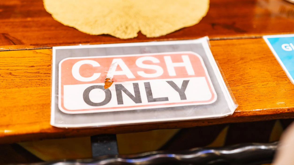 A printed cash only sign in a plastic sleeve lies on a wooden table