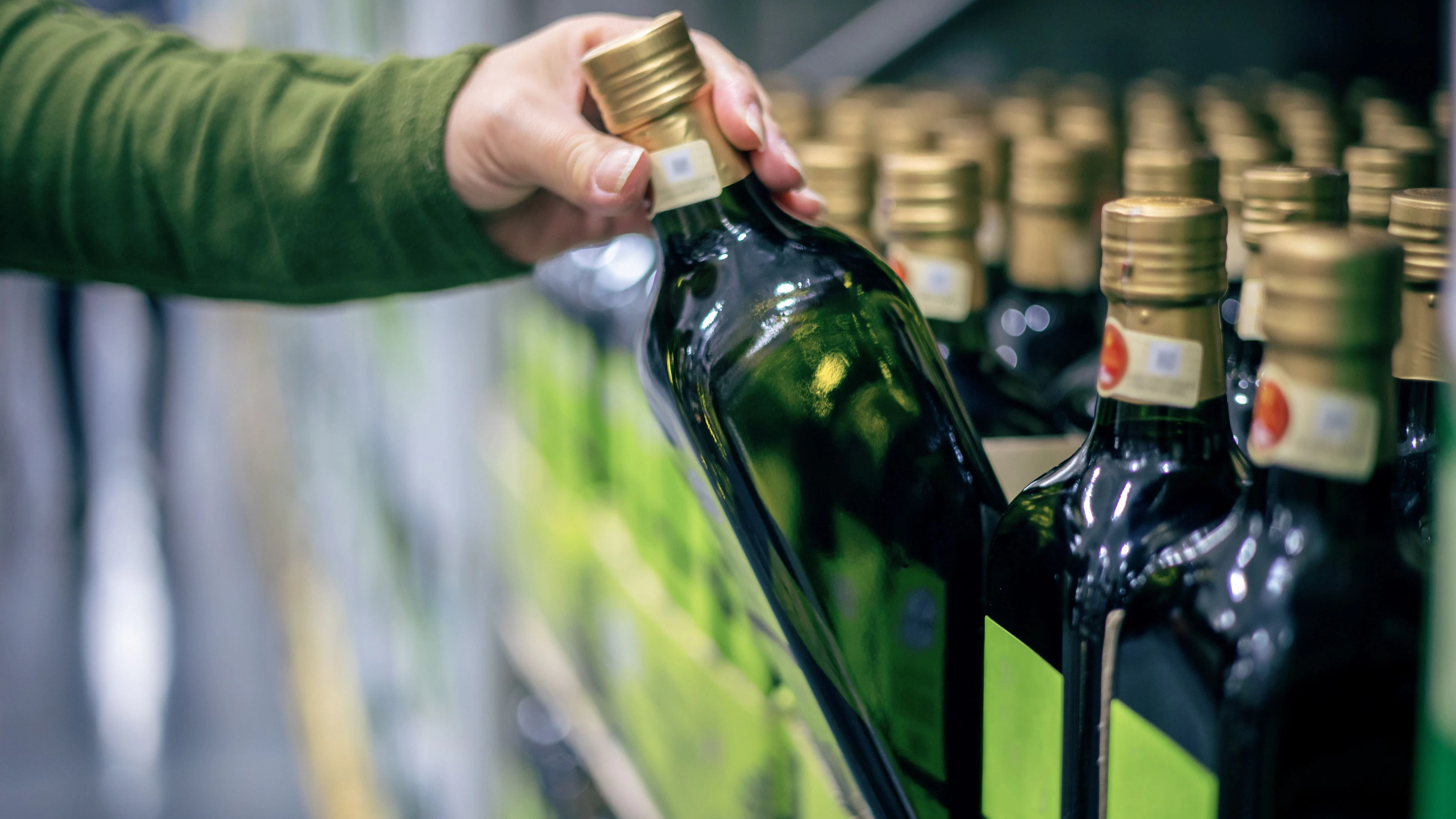 A middle-aged Asian woman selects olive oil at a supermarket, reflecting on healthy eating.