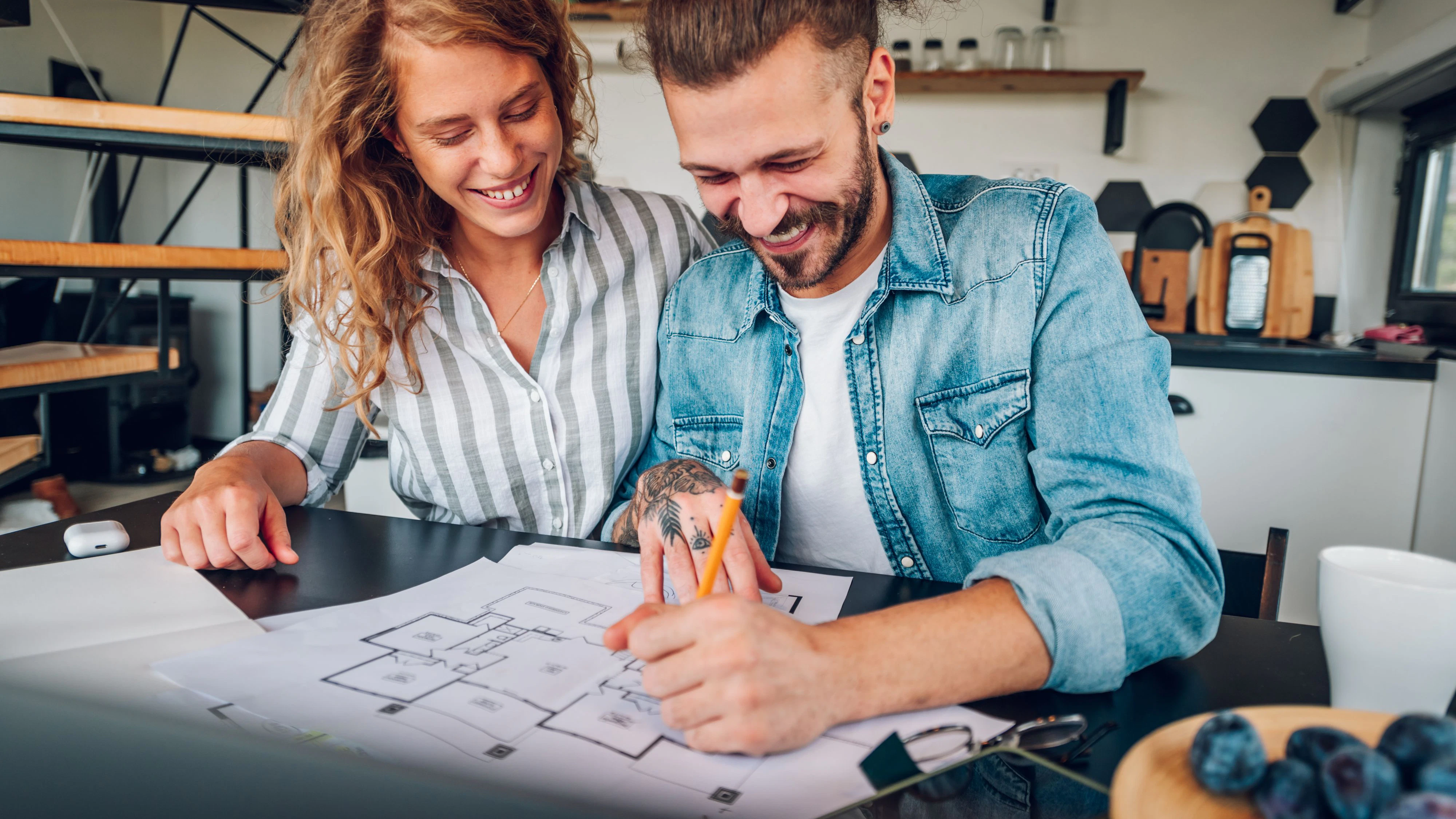 Young couple sitting together in the kitchen at home and looking into the plan of their new house while correcting it before the building starts. Couple is having their first home. Copy space.