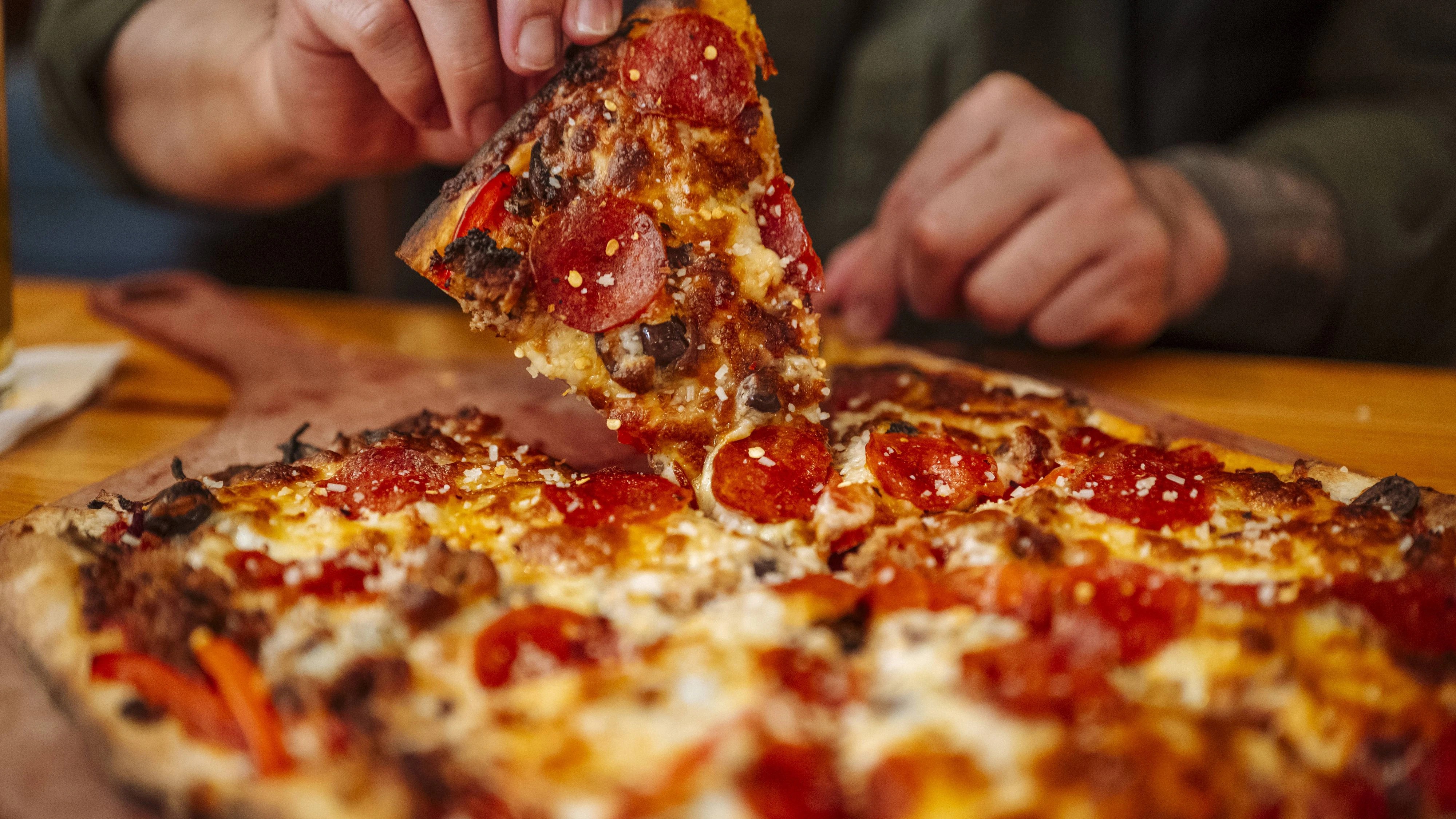 Hand lifting slice of pizza with melted cheese in restaurant. Saint Paul, Minnesota, United States CR_TYRI260427-2008632-01