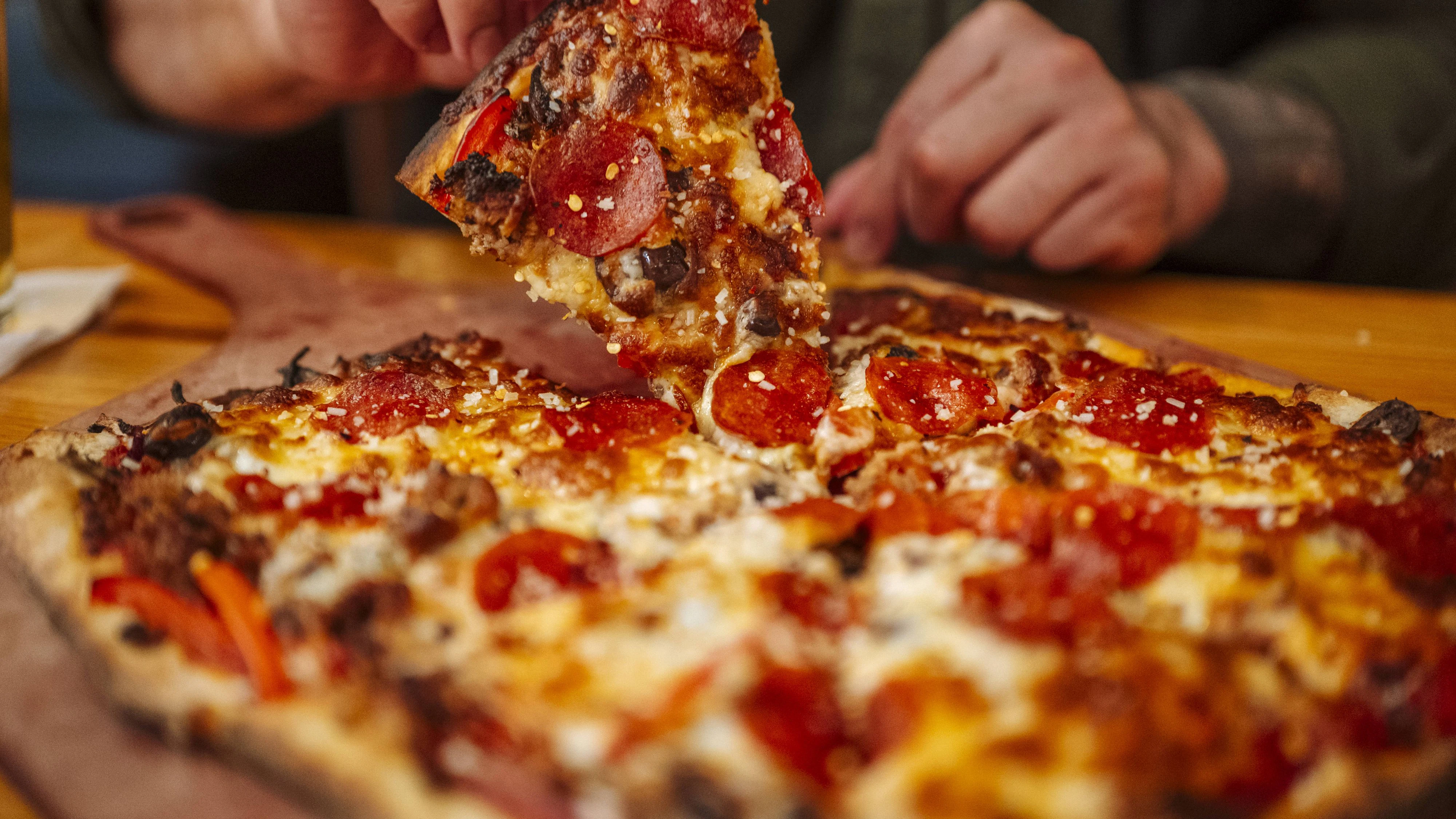 Hand lifting slice of pizza with melted cheese in restaurant. Saint Paul, Minnesota, United States CR_TYRI260427-2008632-01