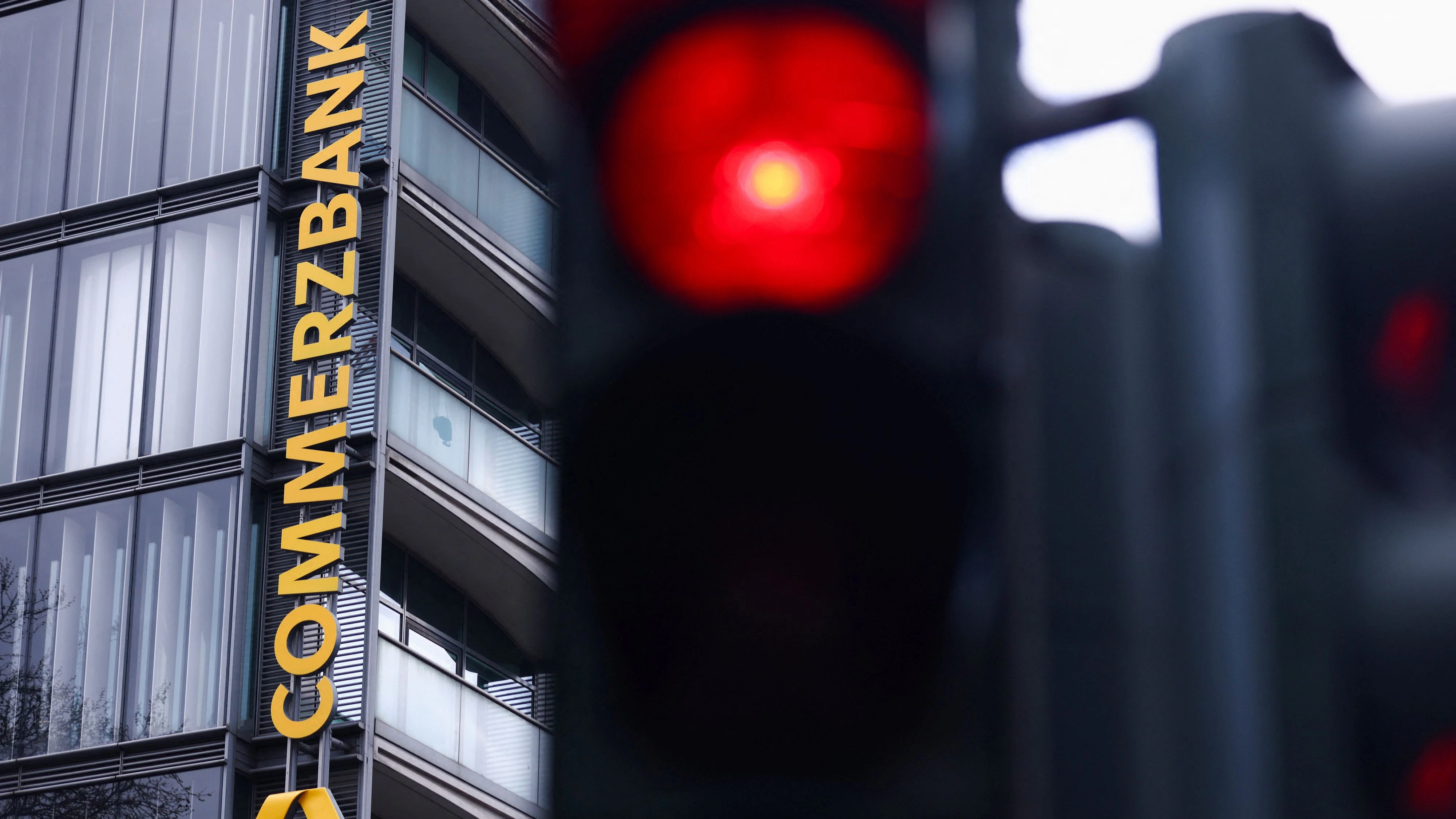 Traffic lights glow near a logo of Commerzbank at a branch as Italy's UniCredit launches an unsolicited bid to increase its stake above 30% in Commerzbank, crossing the mandatory 30% takeover threshold under German law, in Cologne, Germany, March 16, 2026. REUTERS/Thilo Schmuelgen