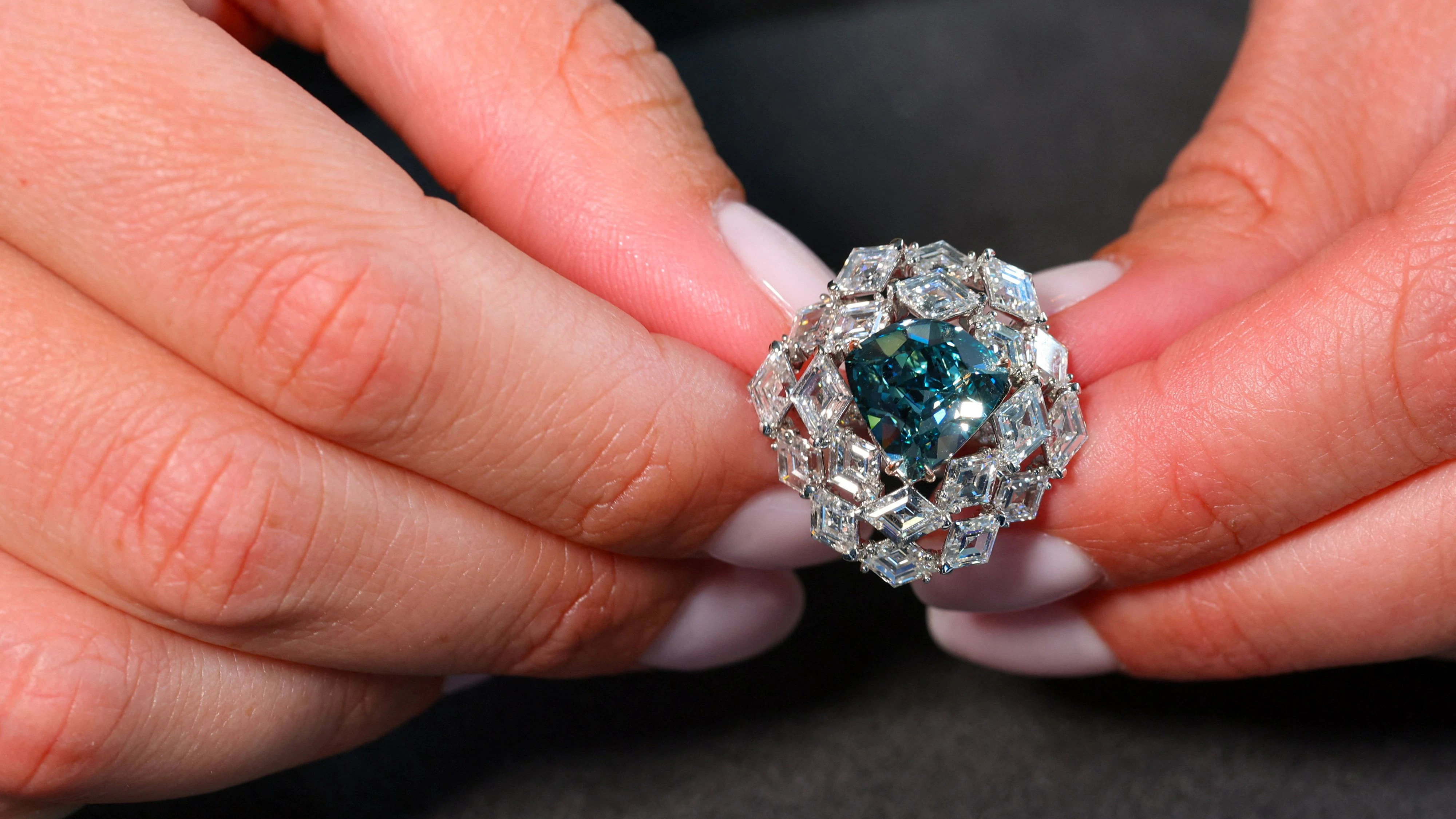 A Christie’s staff member poses with the Ocean Dream, the largest vivid green‑blue diamond, weighing 5.50 carats and estimated at 7–10 million Swiss francs ($9-12.8 million), during an auction preview in Geneva, Switzerland, May 7, 2026. REUTERS/Denis Balibouse