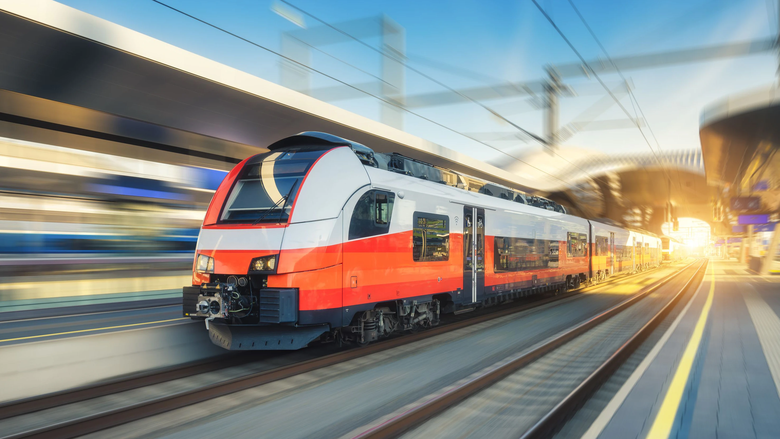 High-speed orange passenger train moving at railway station platform at sunset. Train station. Modern railway transportation concept with blurred motion effect. Railroad. Commercial transport