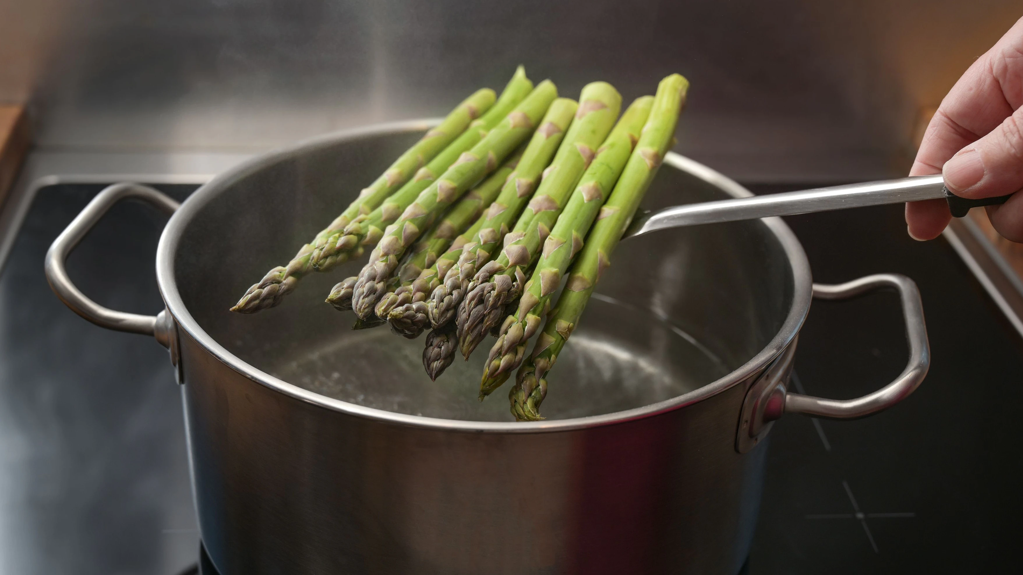 Hand puts green asparagus on a skimmer in a pot with boiling water for a holiday dinner, healthy cooking concept, copy space, selected focus, narrow depth of field