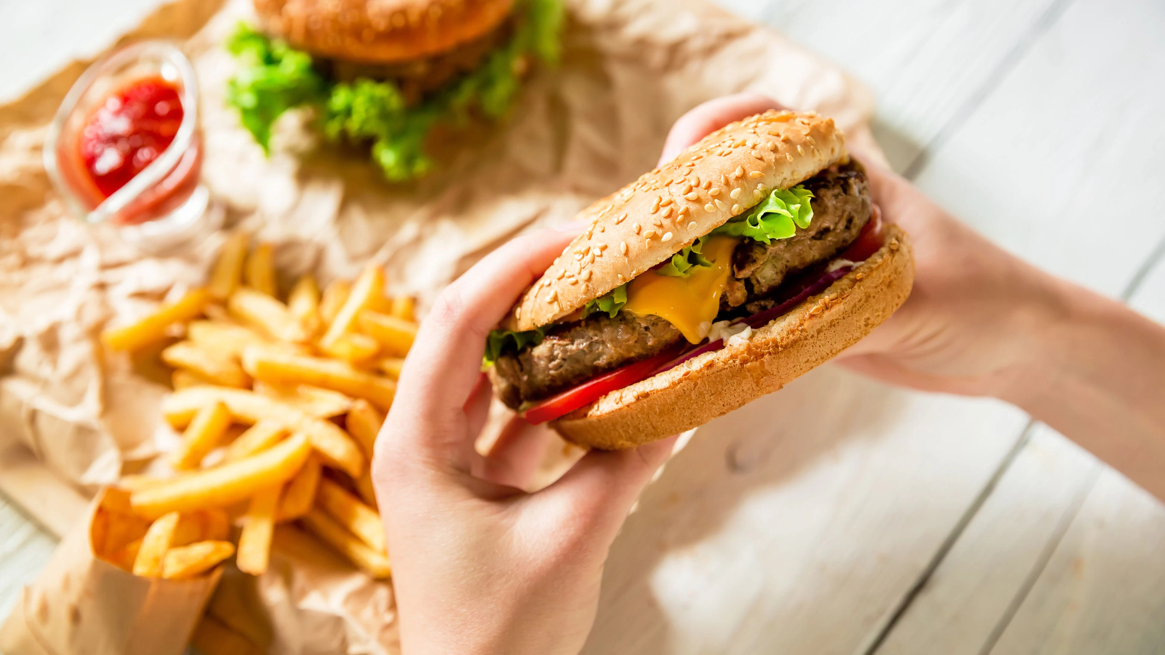 Woman hands holding american tasty burger and french fries, sauce on the wooden plate, white table. Flat lay. Top view