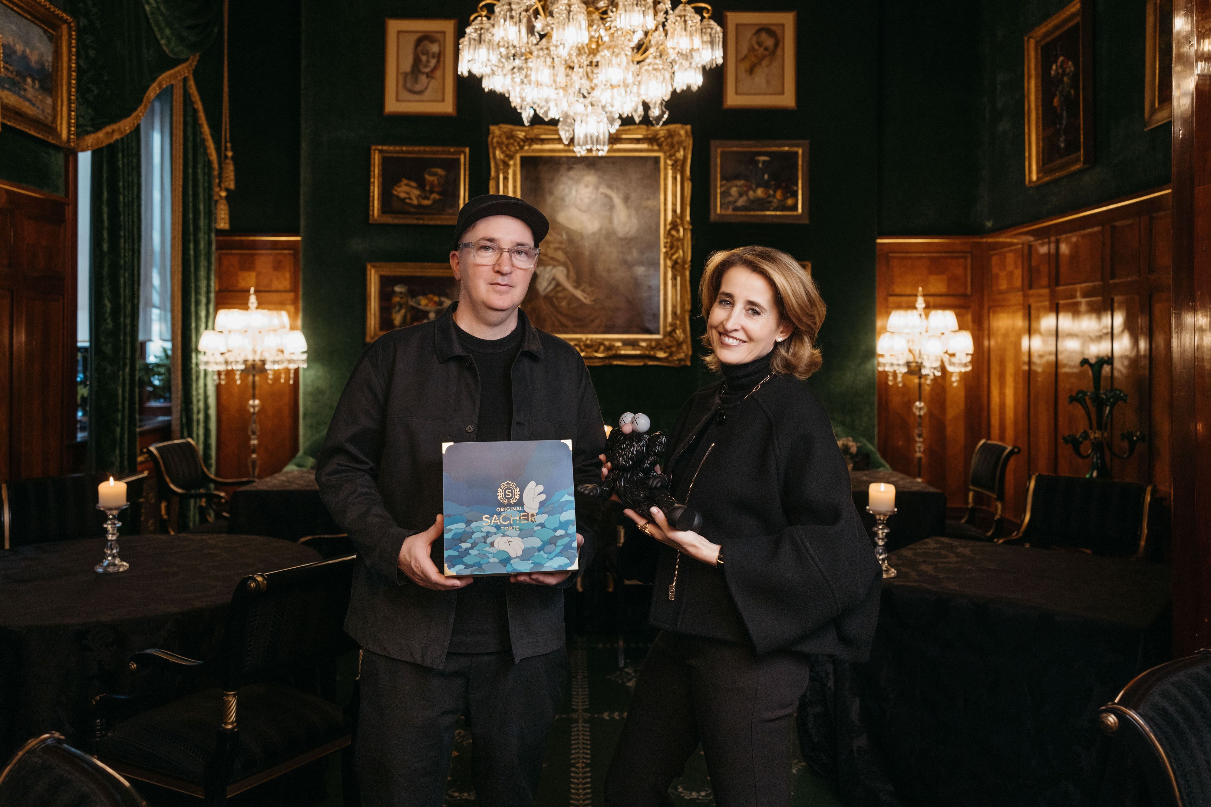 KAWS und Alexandra Winkler, Sacher Co-Eigentümerin (v.l.) päsentieren die neue Sacher-Holzkiste.