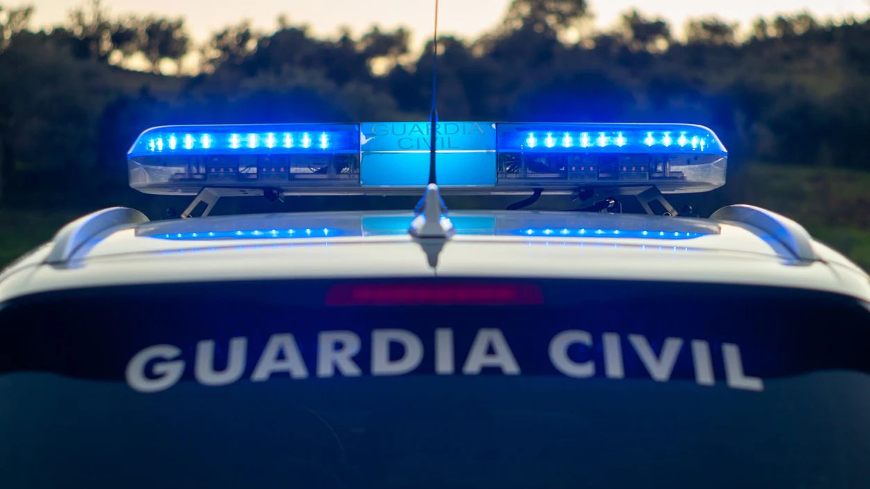 Fotografía al atardecer de un coche de la guardia civil con el puente de señales encendido.