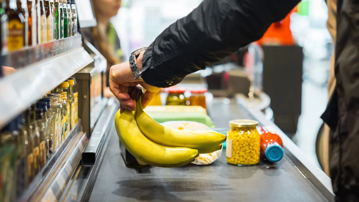 A person putting some bananas and other groceries on the conveyor at a store checkout.