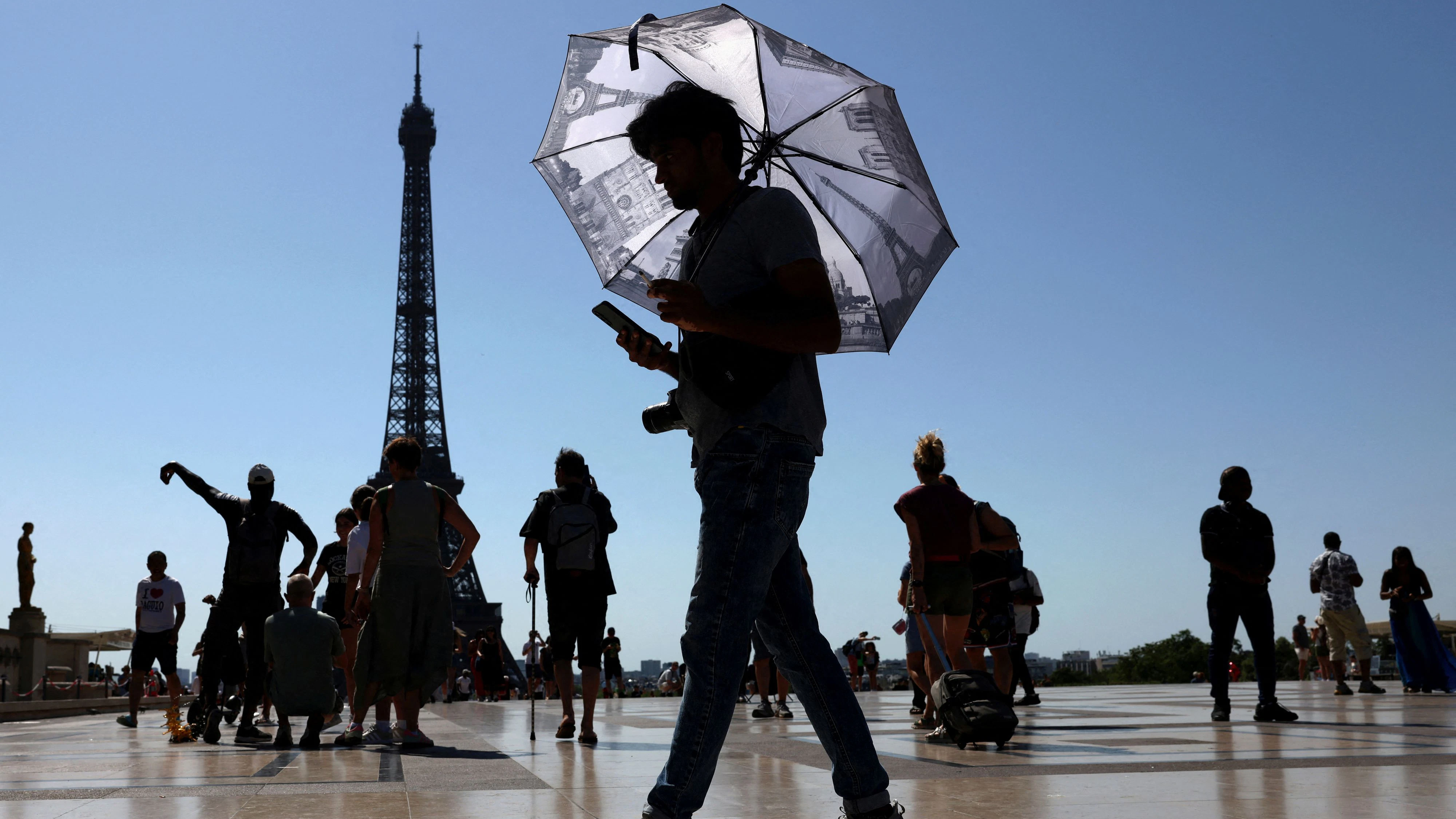 A tourist holding an umbrella to protect himself from the sun walks at Trocadero square next to the Eiffel Tower as an early summer heatwave hits Paris, France, July 1, 2025. REUTERS/Tom Nicholson     TPX IMAGES OF THE DAY     
