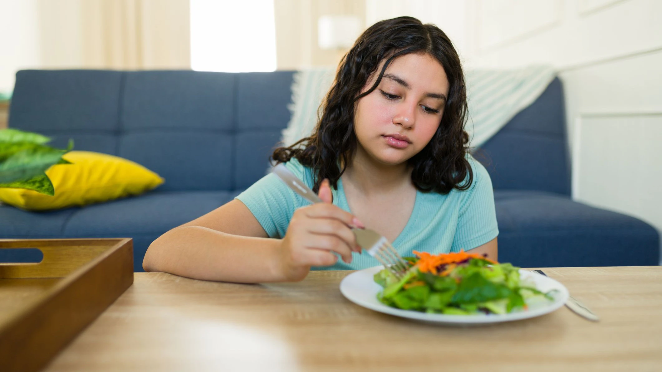 Unwilling teenage girl eating a healthy salad at home, grappling with eating disorder and health issues, highlighting the connection between diet and mental health