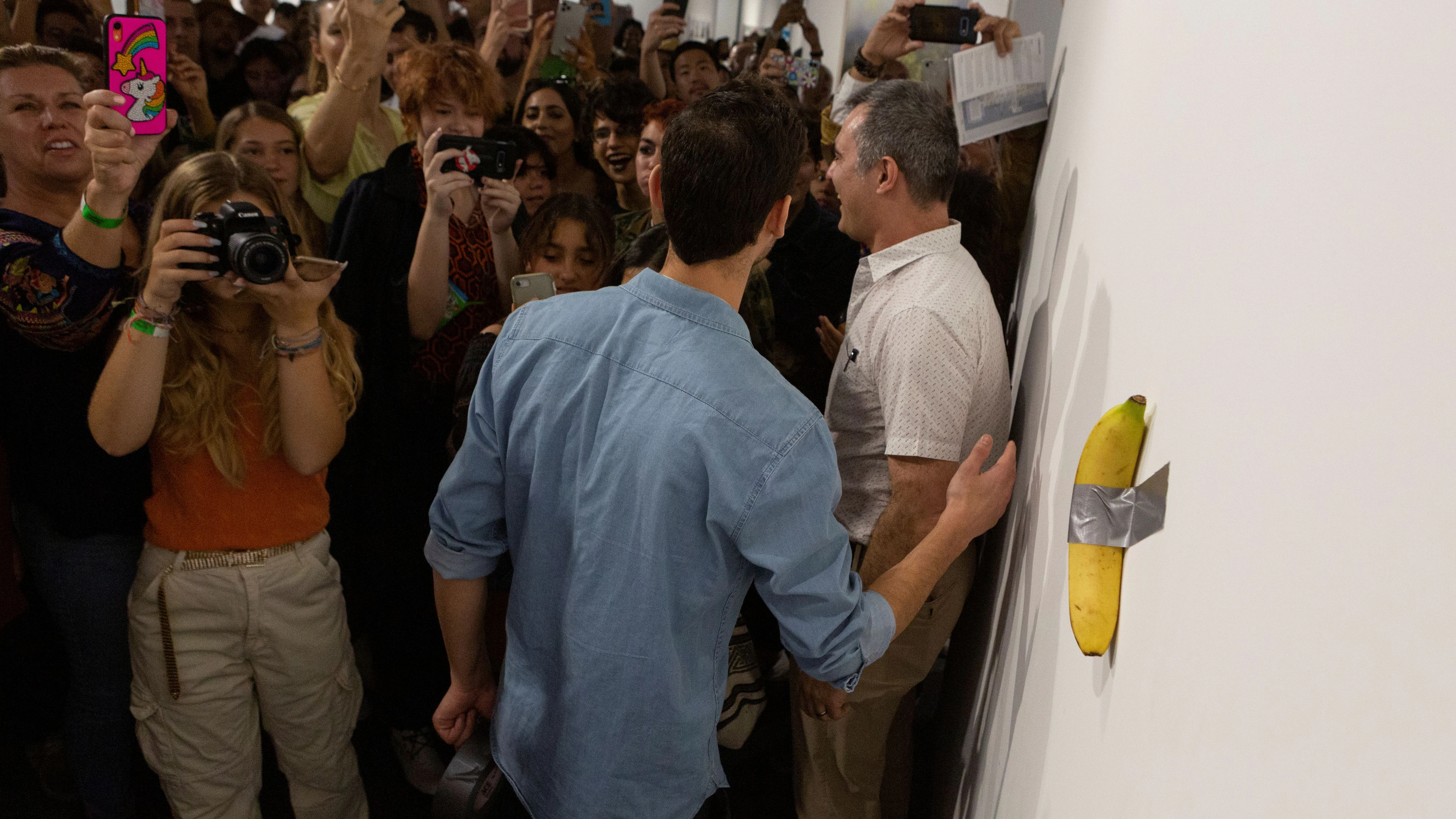 Art Basel visitors use their phones in front of a banana attached with duct-tape that replaces the artwork 'Comedian' by the artist Maurizio Cattelan, which was eaten by David Datuna, in Miami Beach, Florida, December 7, 2019.  REUTERS/Eva Marie Uzcategui