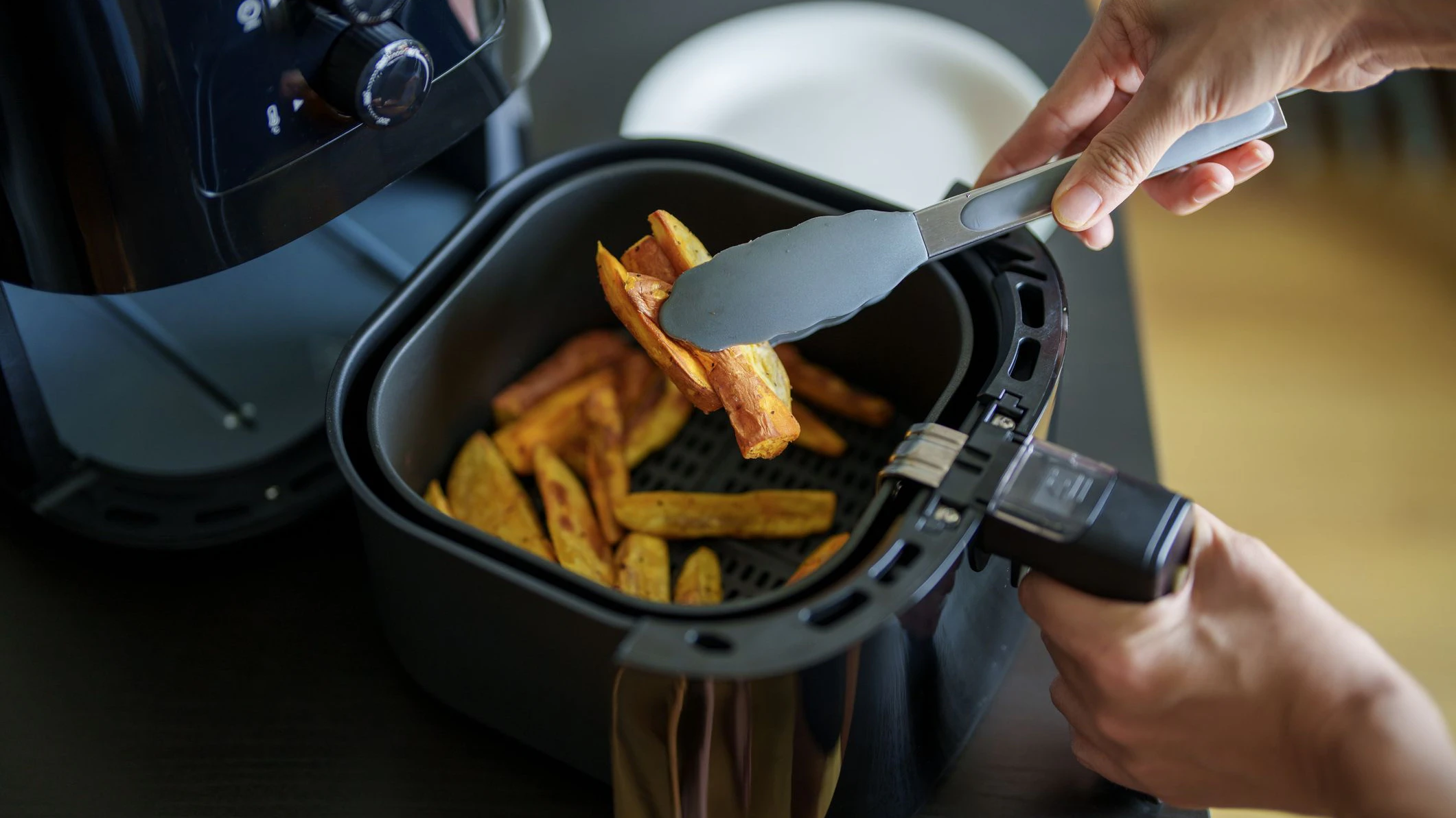 A woman is using an air fryer to prepare food in her kitchen, focusing on a healthier cooking method with minimal oil.