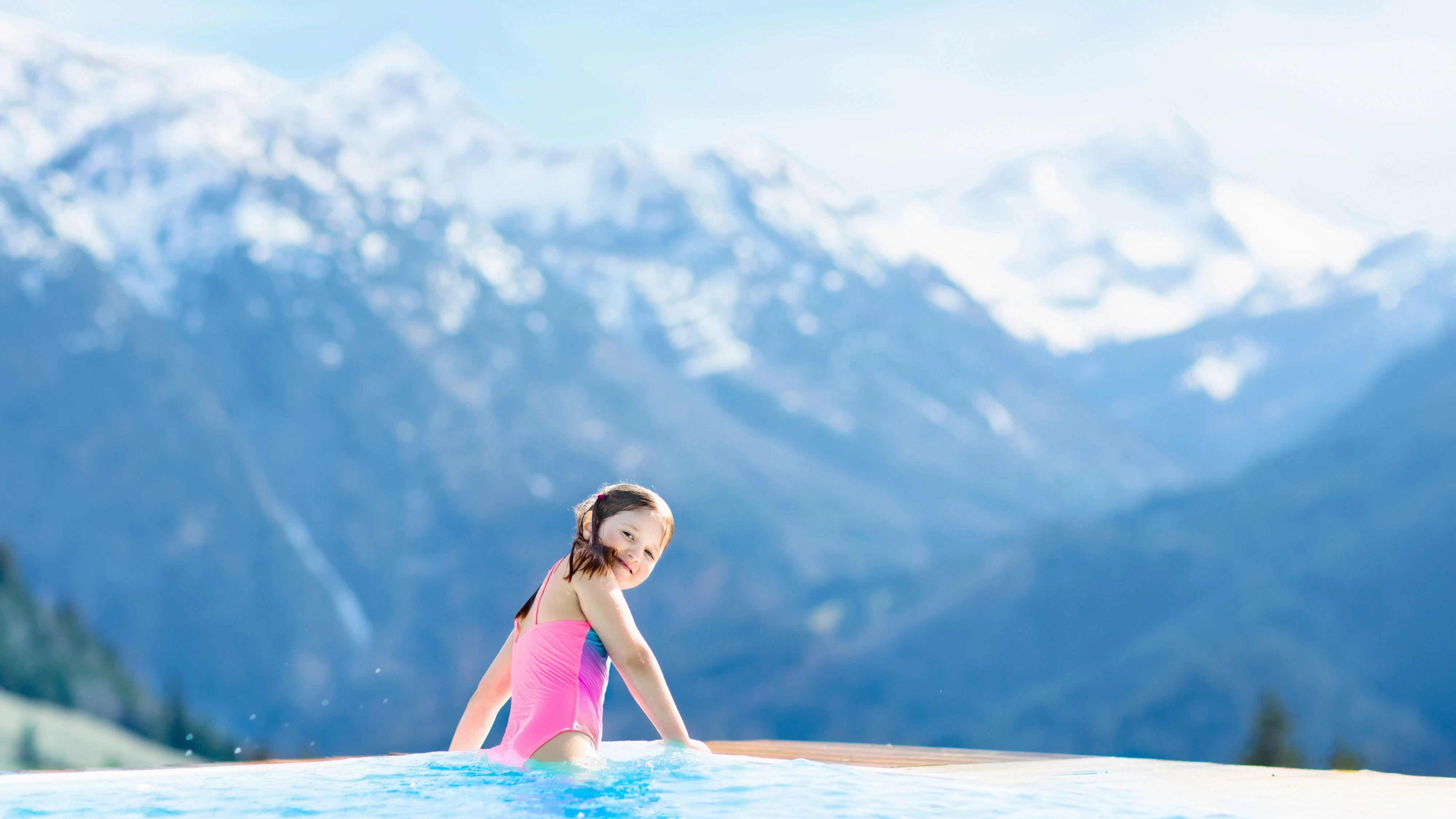 Child in outdoor infinity pool with snowy mountain in the background. Family vacation in luxury Alpine resort. Kids in the Alps mountains. Hot tub in snow. Apres ski activity for kids. Children swim. model released