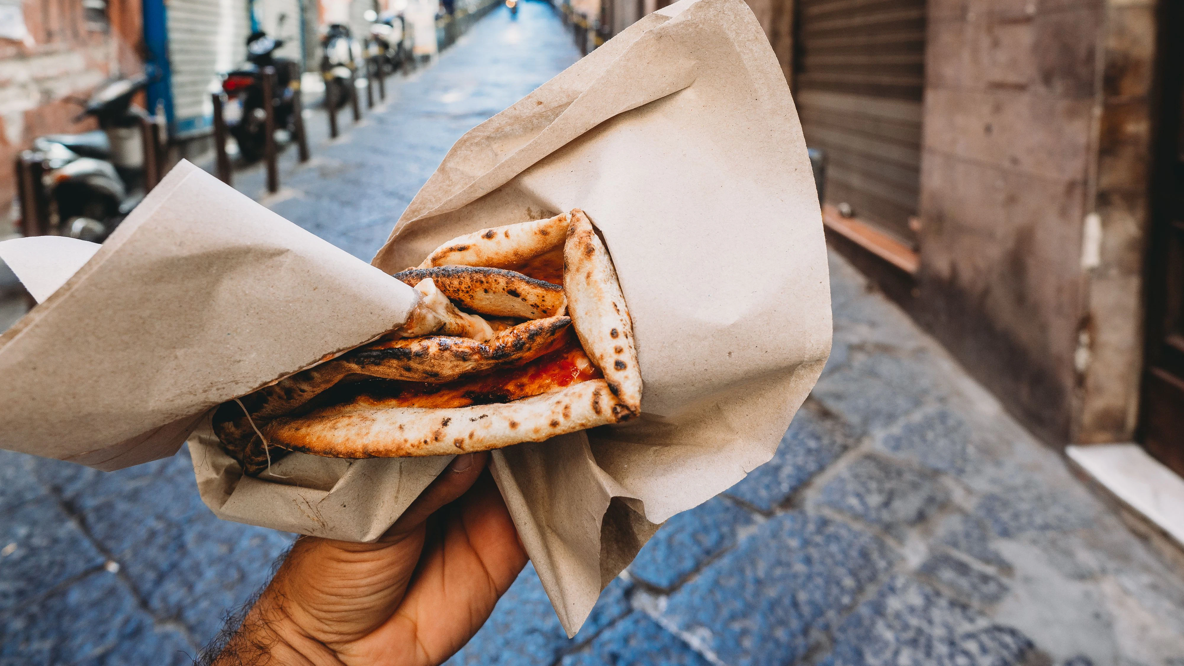Pov view of a man eating a typical "Pizza a portafoglio" in Naples, Italy. The man is holding the wallet pizza.