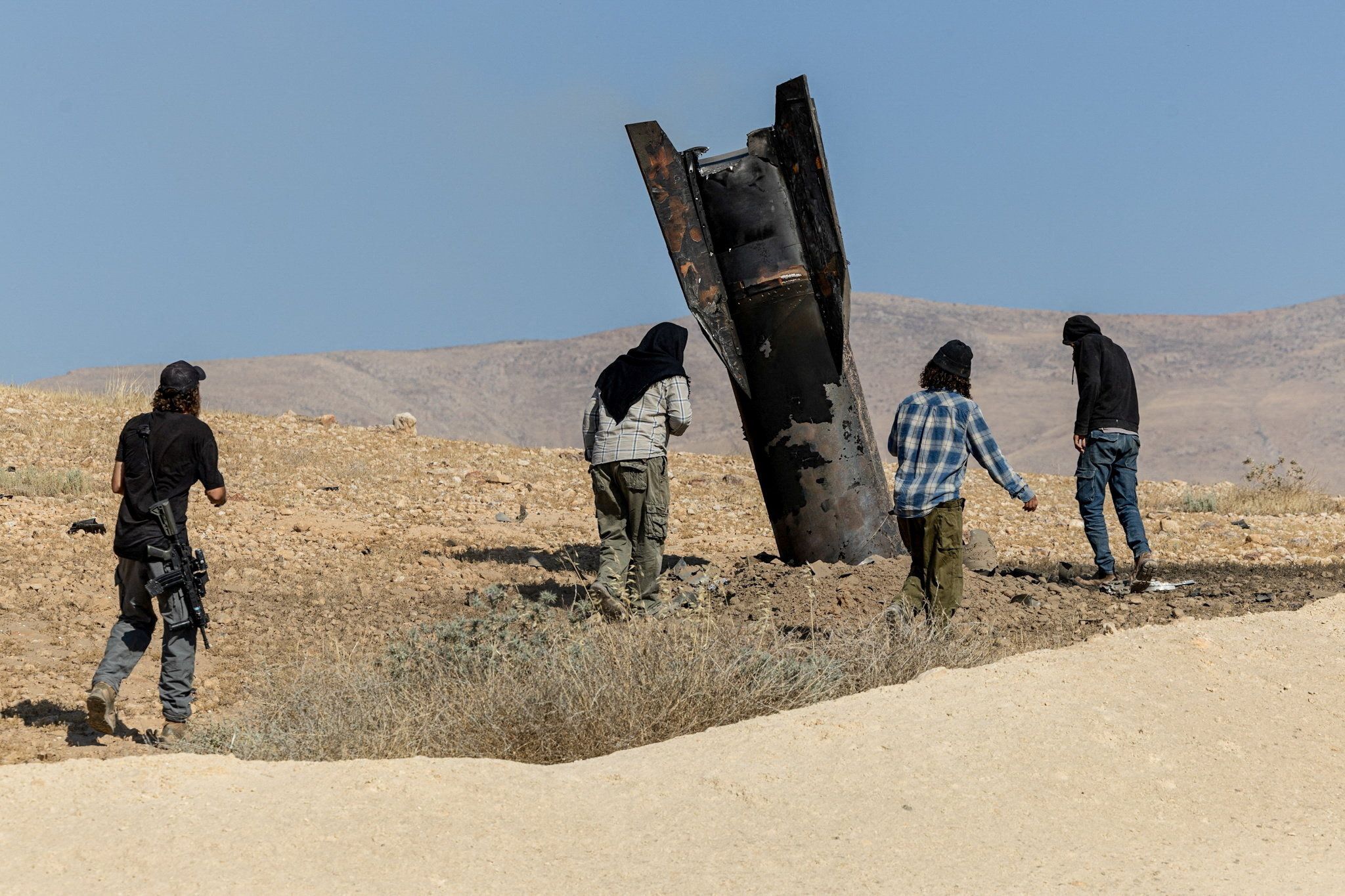 Israelische Siedler stehen neben einem Teil einer Rakete, der nach iranischen Angriffen aus dem Boden ragt, im zentralen israelisch besetzten Westjordanland, 8. Juni 2026.