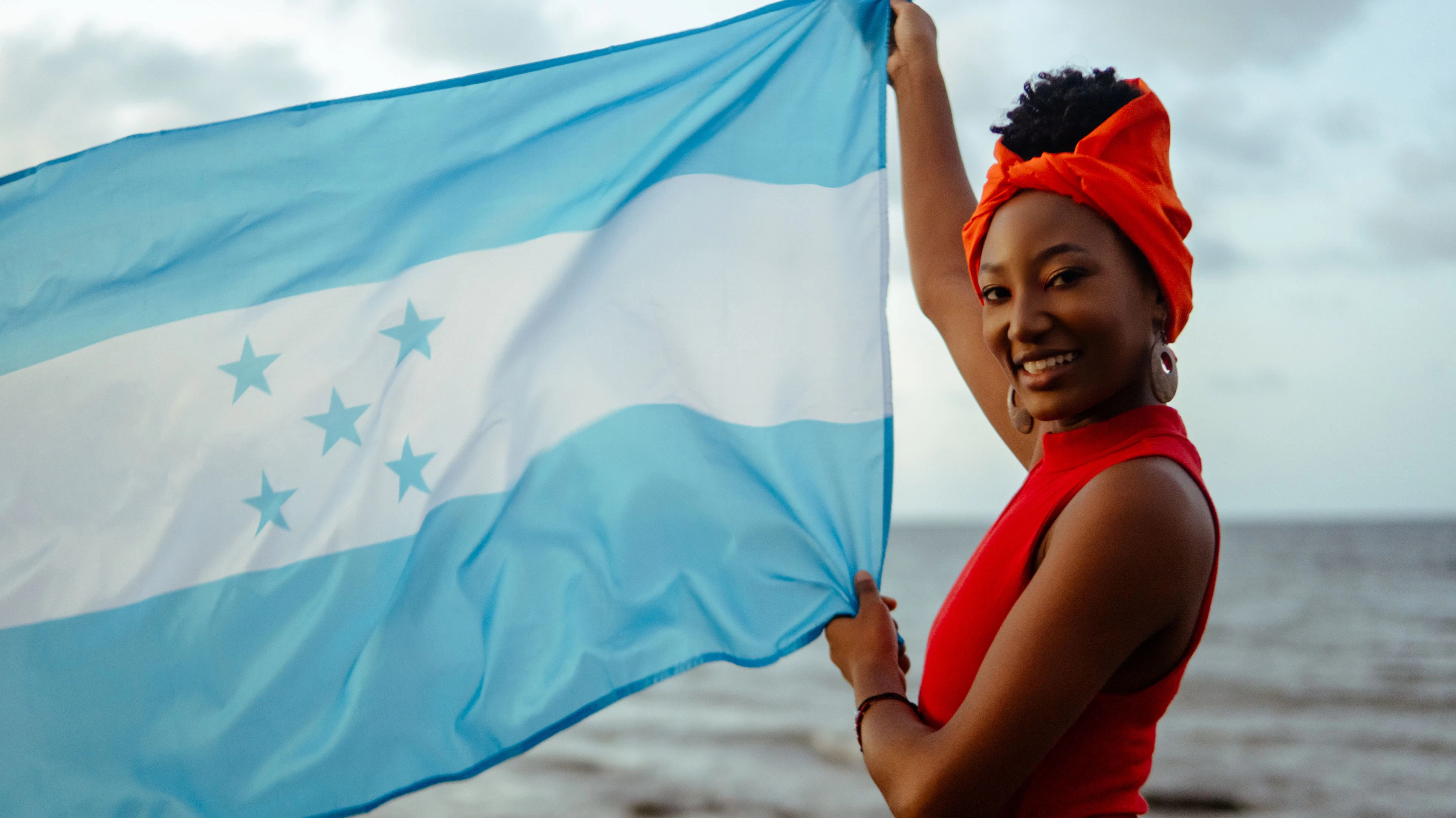 Young garifuna woman proudly displaying the honduran flag by the sea
