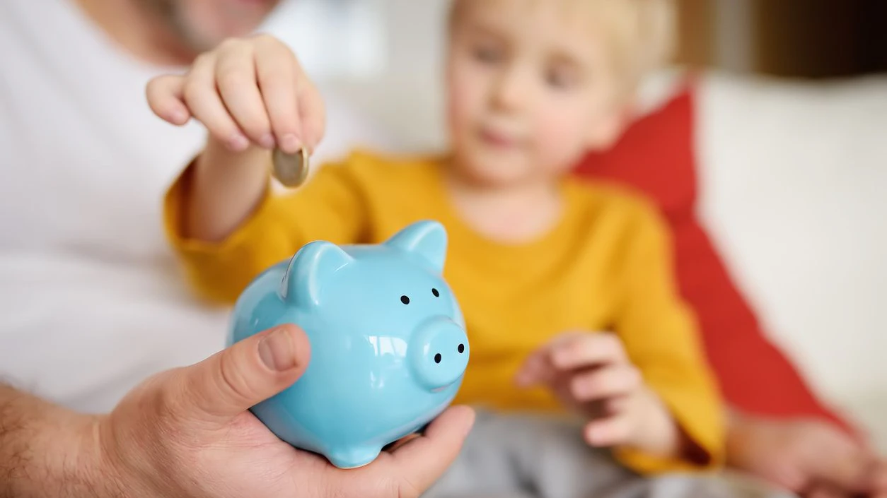 Father and son putting coin into piggy bank. Education of children in financial literacy