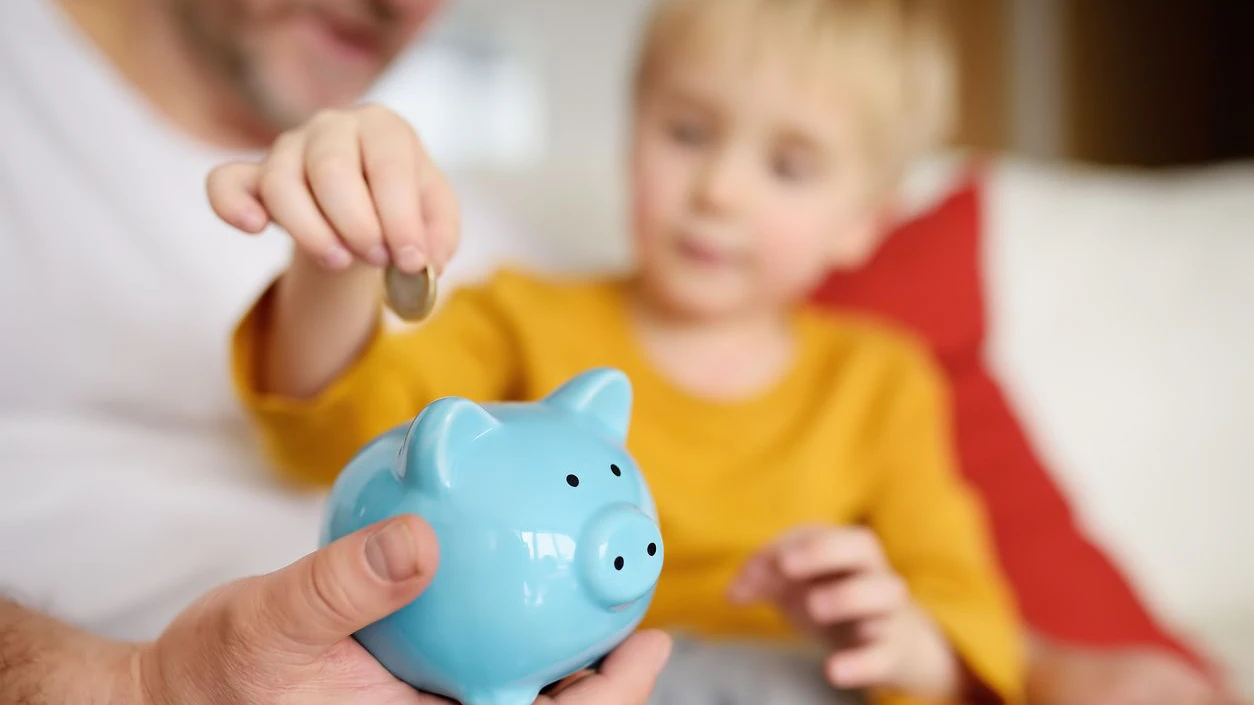 Father and son putting coin into piggy bank. Education of children in financial literacy