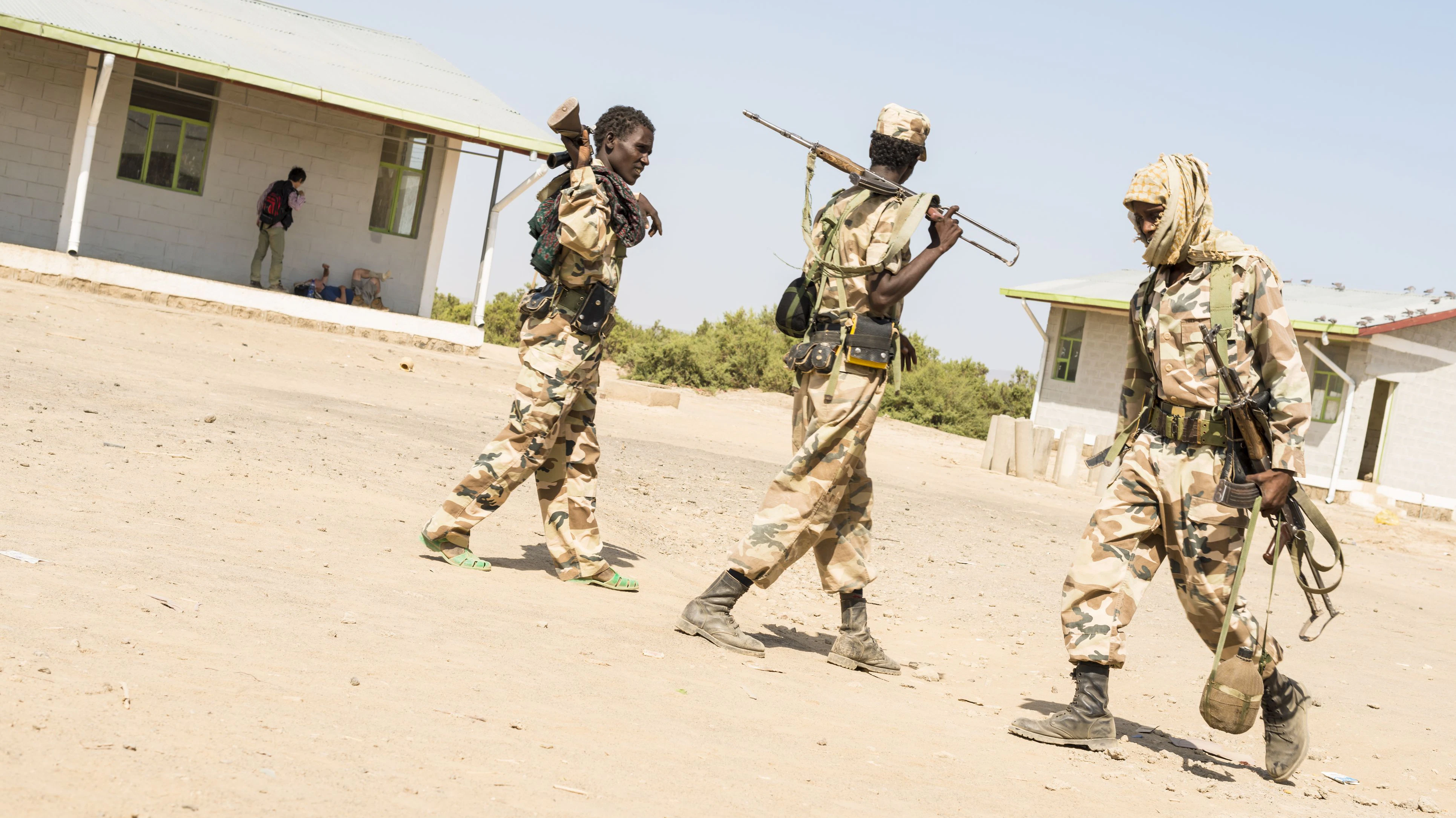 "Mek'ele, Ethiopia - November 9, 2012: Afar soldiers. Three Afar soldiers in uniforms walking throe a dirt courtyard. They have Kalashnikov on their shoulders. At the background two wooden office buildings and some tourists waiting."