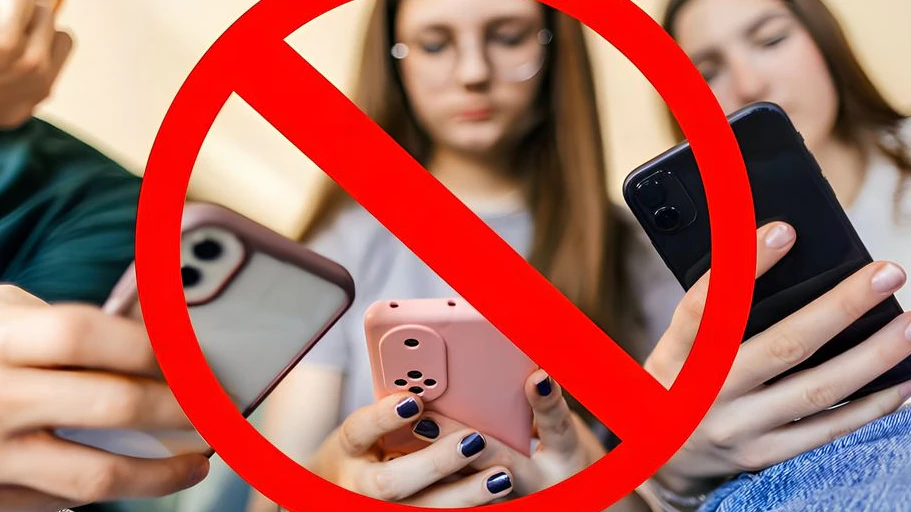 One teenage boy and two teenage girls have fun together using mobile phones at home. Beautiful young people are friends and high school students.