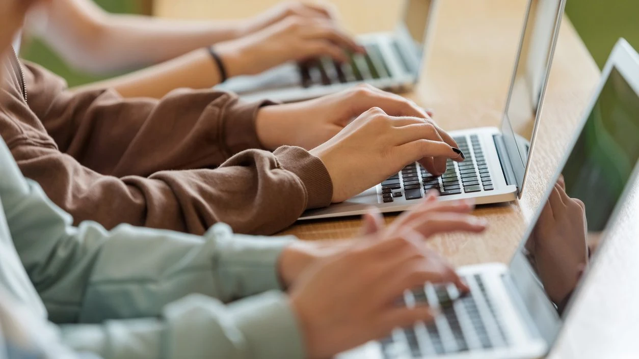 High school students sitting at the desk in the classroom during lesson, using laptops. Close up of hands, unrecognizable people.