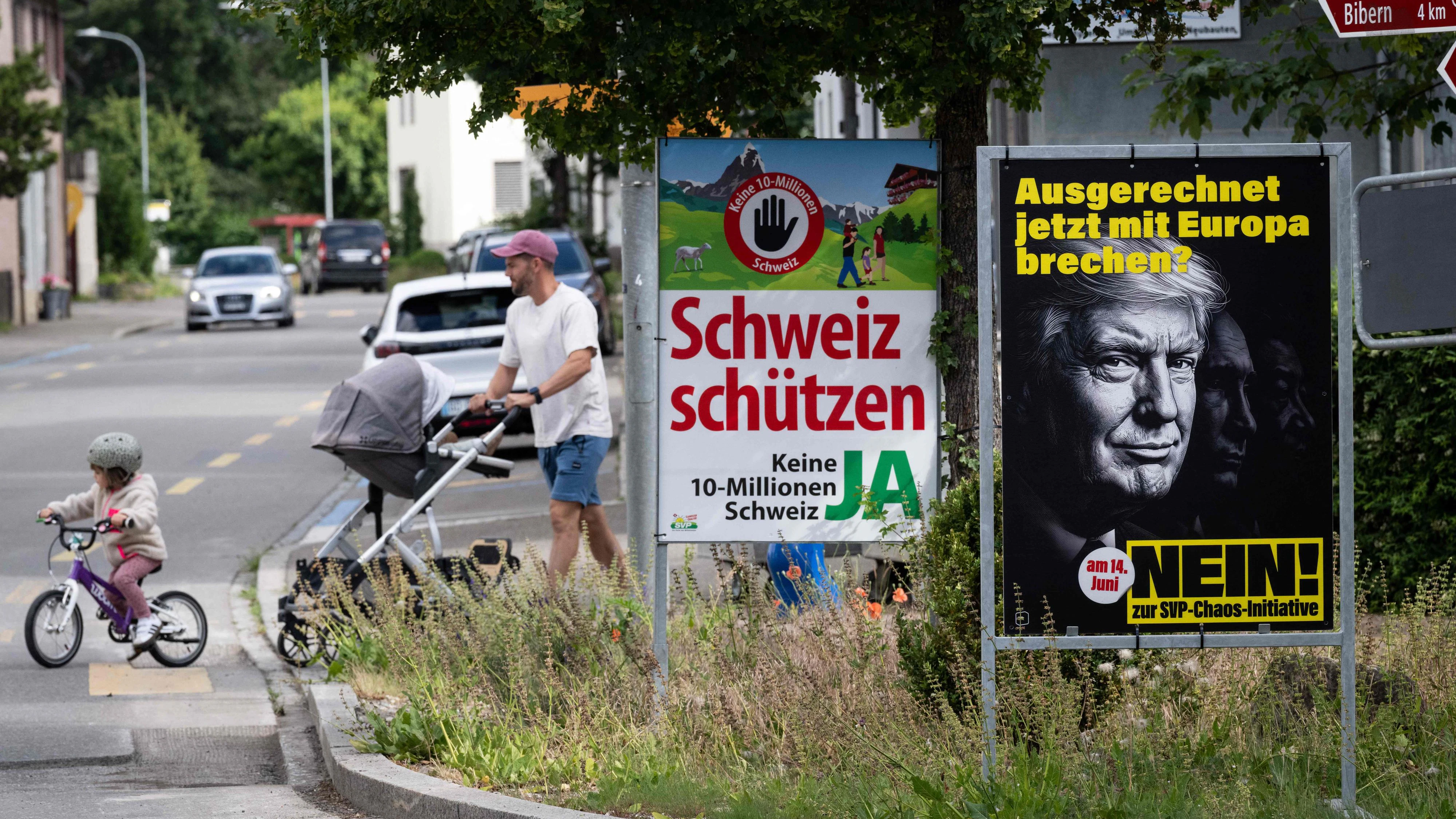 Pedestrians walks past posters campaigning to vote in an upcoming an anti-immigration initiave launched by the Swiss People's Party (SVP) and reading "Protect Swizterland, no to a Switzerland of 10 million - YES" and "Breaking with Europe now of all times ? - NO on the SVP-Chaos-Initiative" in Thayngen, northern Switzerland, on June 1, 2026. The Swiss will vote on June 14, 2026, on an initiative to cap the population at 10 million -- an anti-immigration proposal that is fracturing public opinion in the wealthy Alpine nation. "No to a Switzerland of 10 million inhabitants," is the name of the project launched by the country's biggest party, the hard-right Swiss People's Party (SVP), renowned for its opposition to immigration and closer ties with the European Union. (Photo by SEBASTIEN BOZON / AFP)