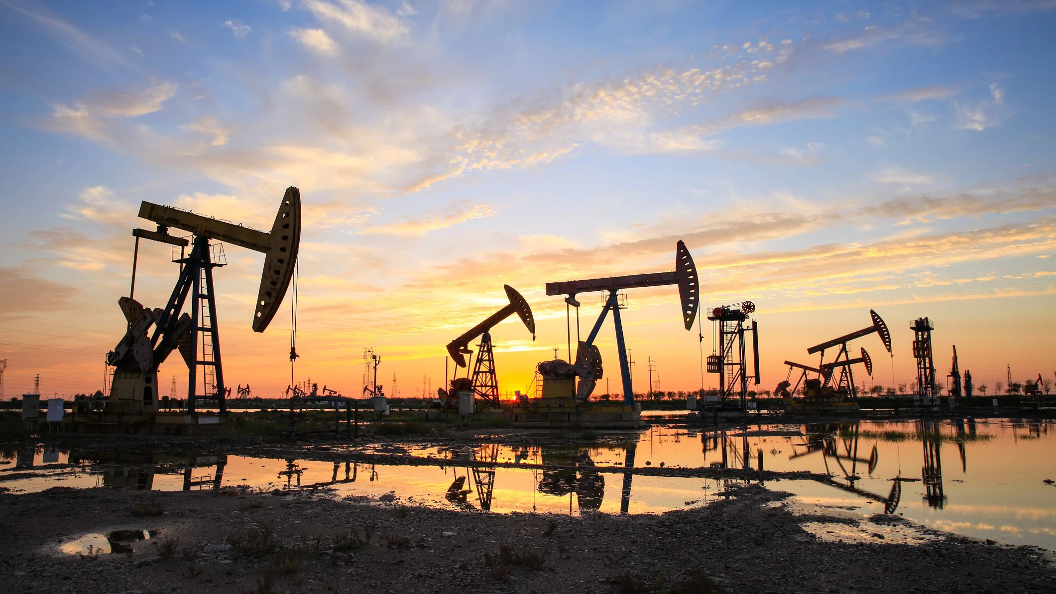 Oil field site, in the evening, oil pumps are running, The oil pump and the beautiful sunset reflected in the water, the silhouette of the beam pumping unit in the evening.