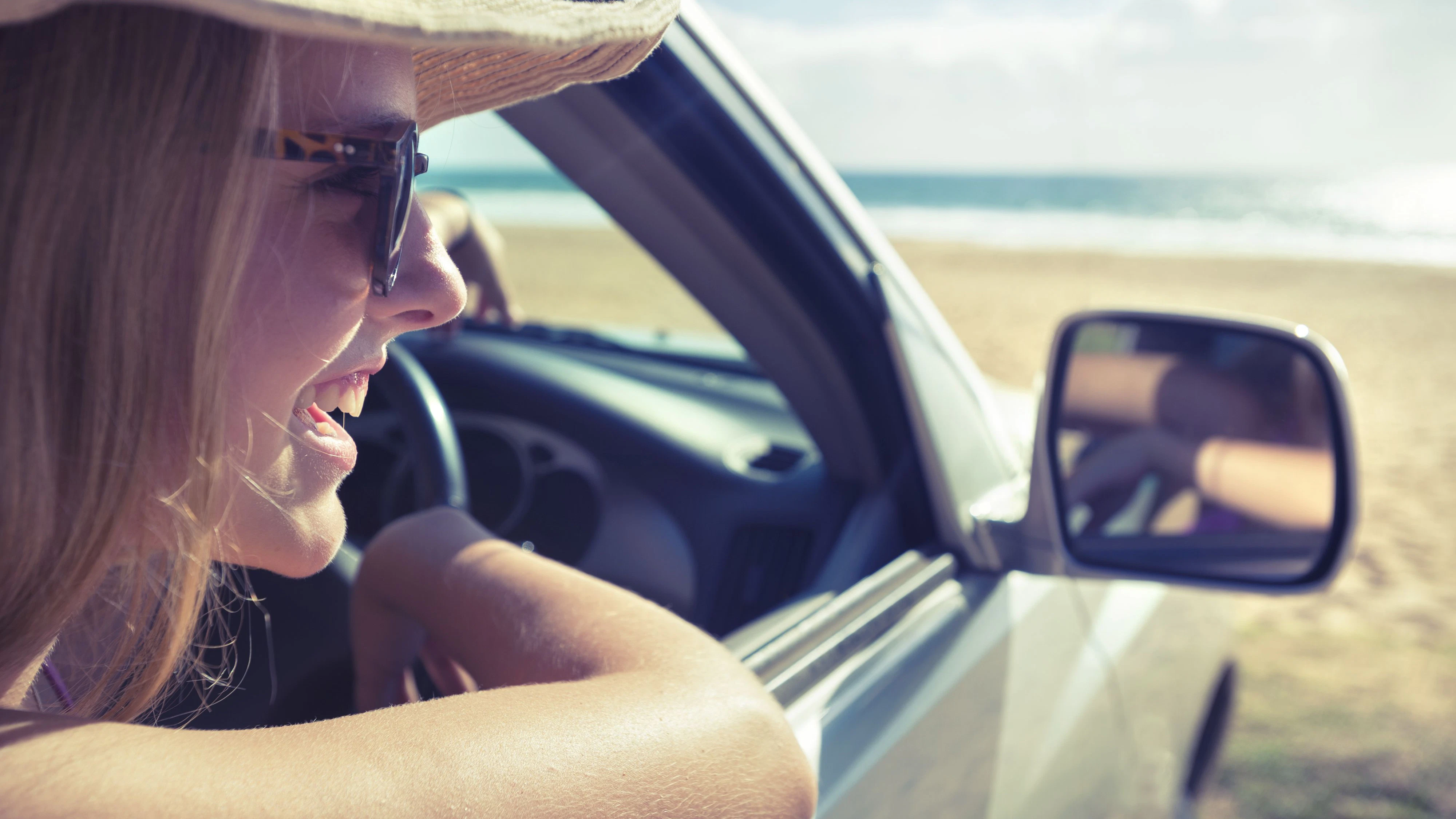 Woman looking out of a car window at the beach on a sunny day