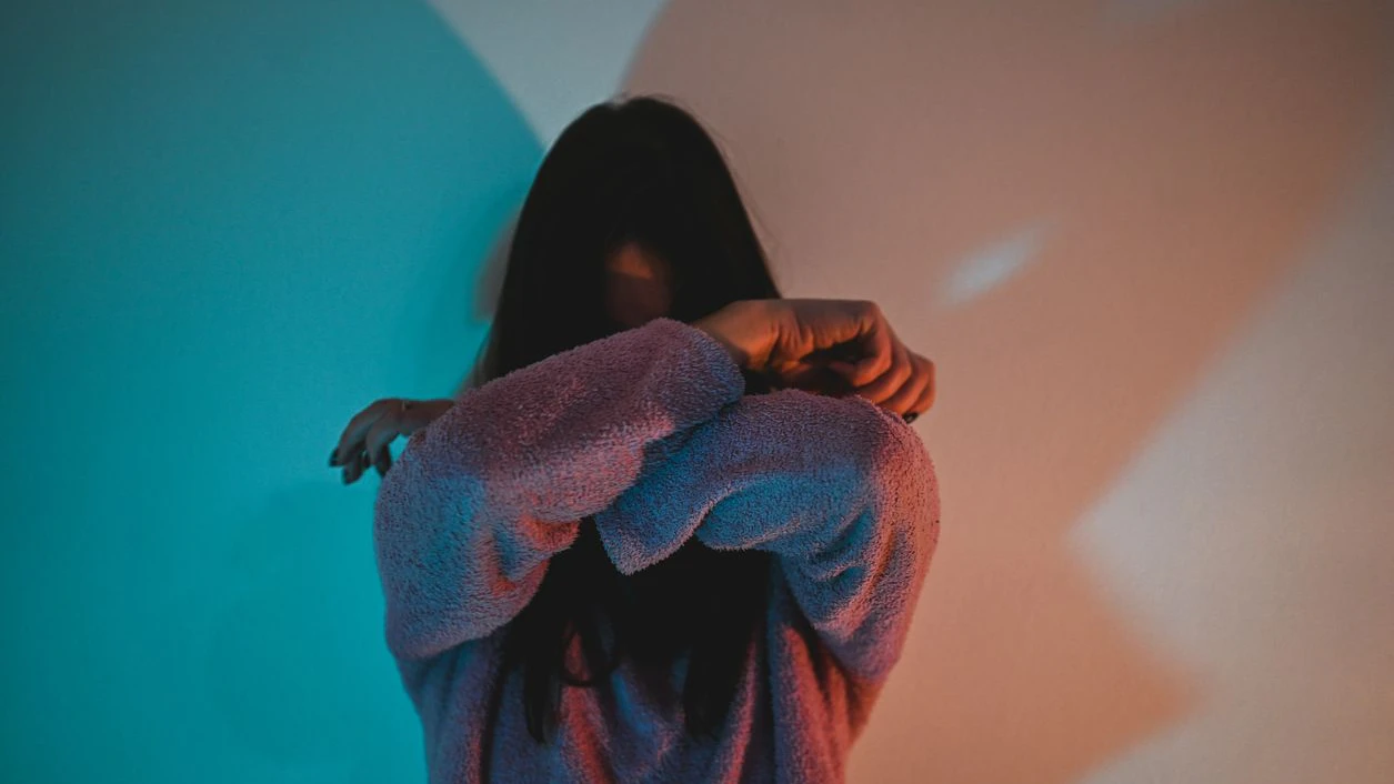 Young woman hiding her face with crossed arms in neon light